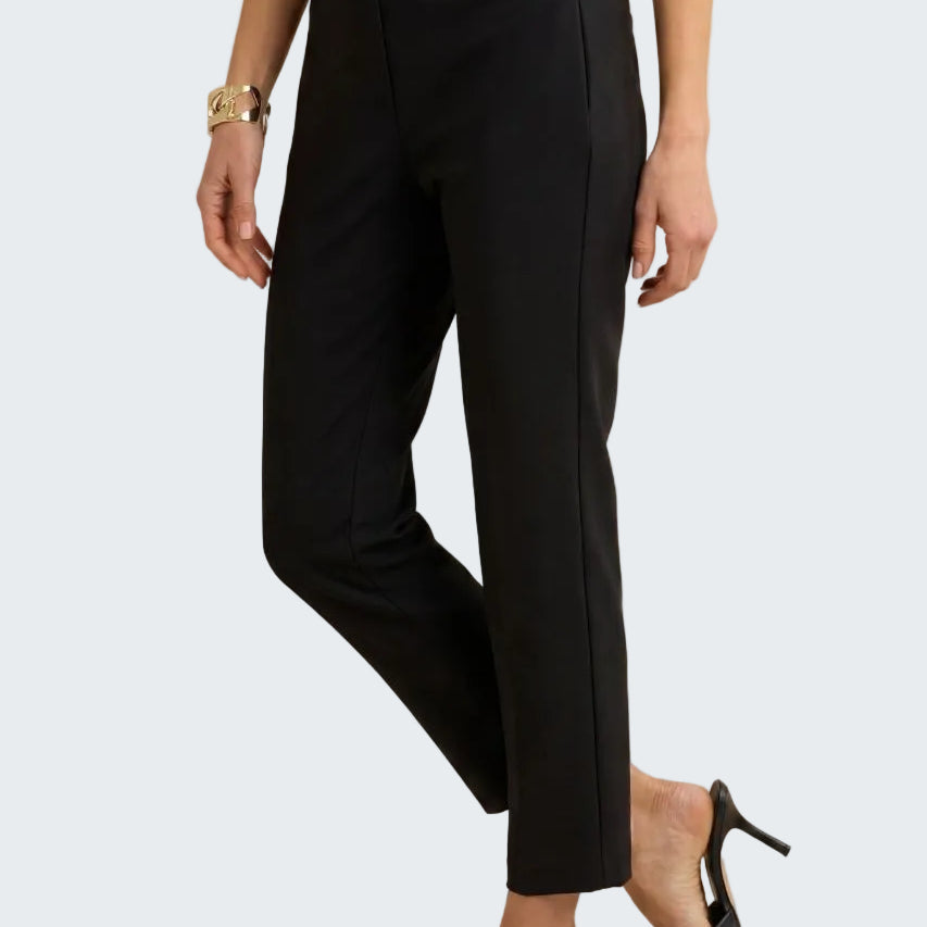 A model wearing black cropped ankle-length trousers with side seam detailing, paired with a white top and black mule heels, against a neutral beige background.