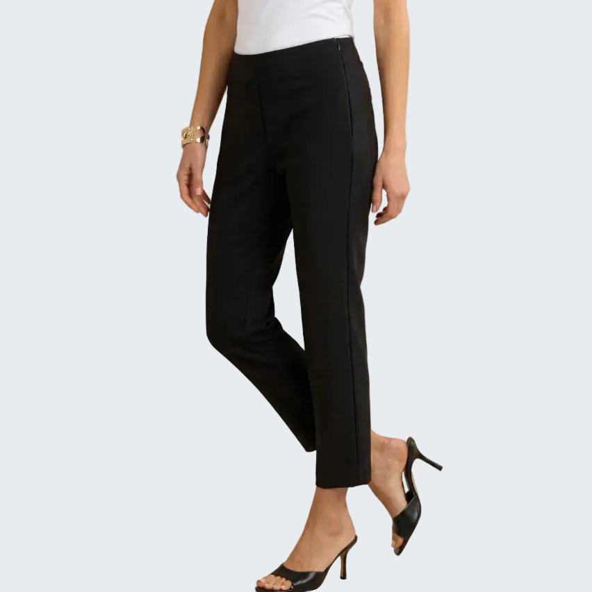 A model wearing black cropped ankle-length trousers with side seam detailing, paired with a white top and black mule heels, against a neutral beige background.