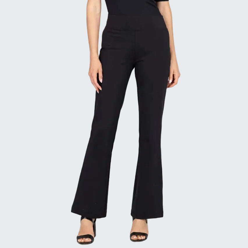 A model wearing black high-waisted flare pants with a smooth texture, paired with black sandals, against a neutral beige textured backdrop.