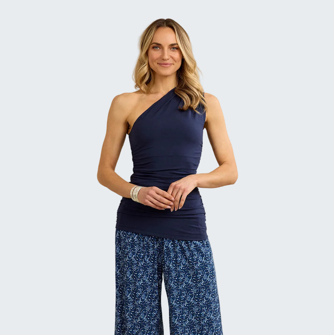 Woman wearing a navy one-shoulder top and blue patterned pants against a beige background
