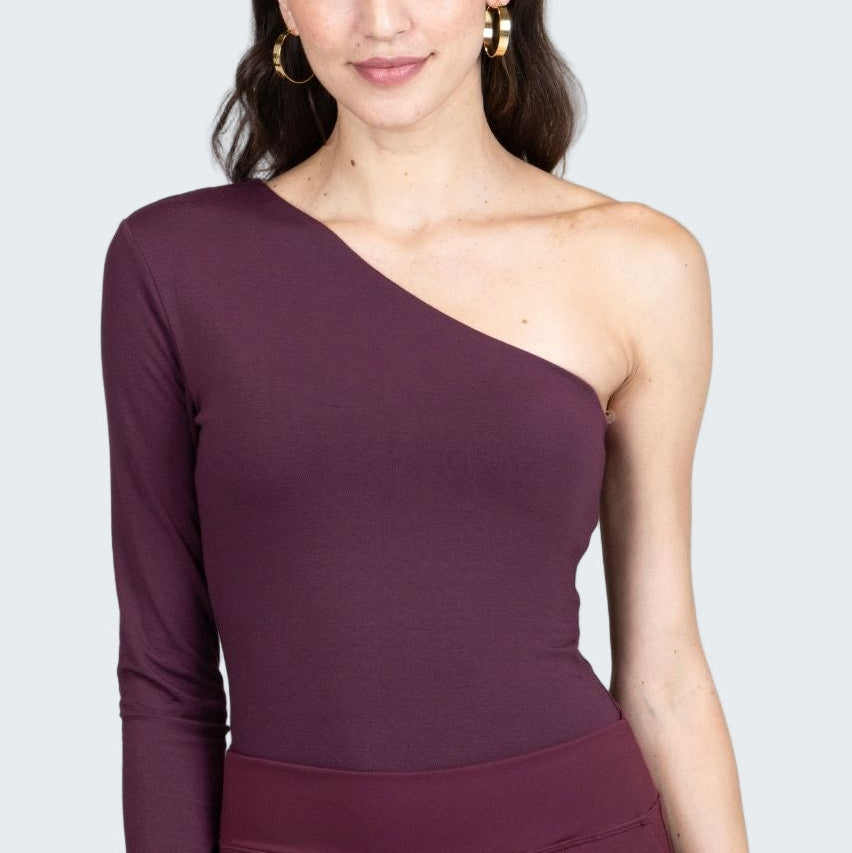 Woman wearing a one-shoulder purple dress against a gray background