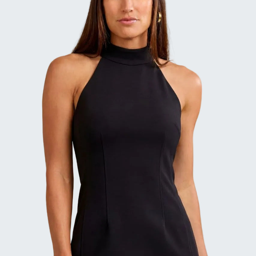 A woman modeling a sleeveless black mock neck top with structured side seams, paired with black pants, against a textured beige background.