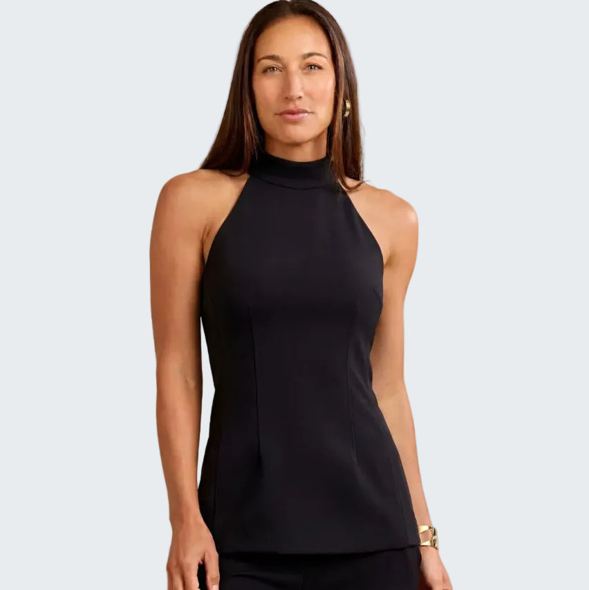 A woman modeling a sleeveless black mock neck top with structured side seams, paired with black pants, against a textured beige background.