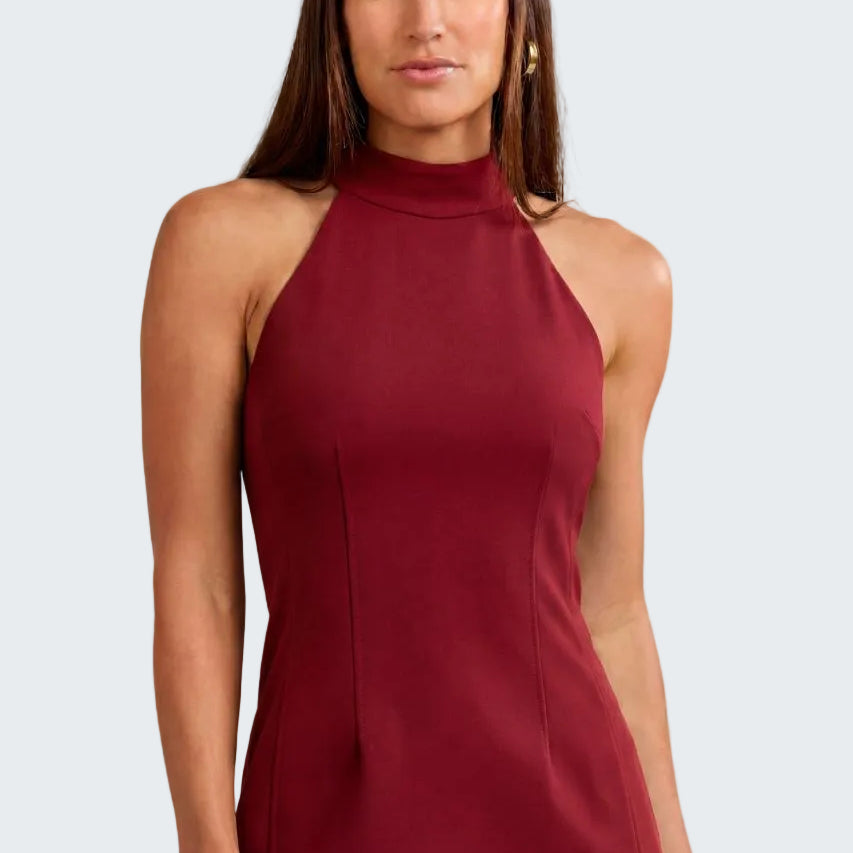 A woman modeling a sleeveless high-neck top and matching pants in a deep burgundy color, set against a neutral textured beige background.