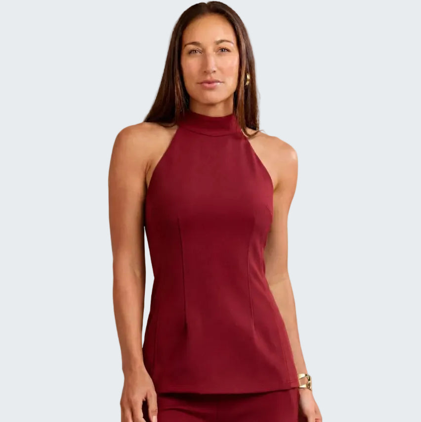 A woman modeling a sleeveless high-neck top and matching pants in a deep burgundy color, set against a neutral textured beige background.