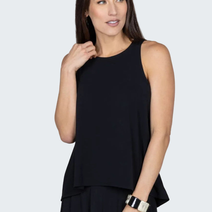 Woman wearing a black sleeveless top and dark pants against a beige background