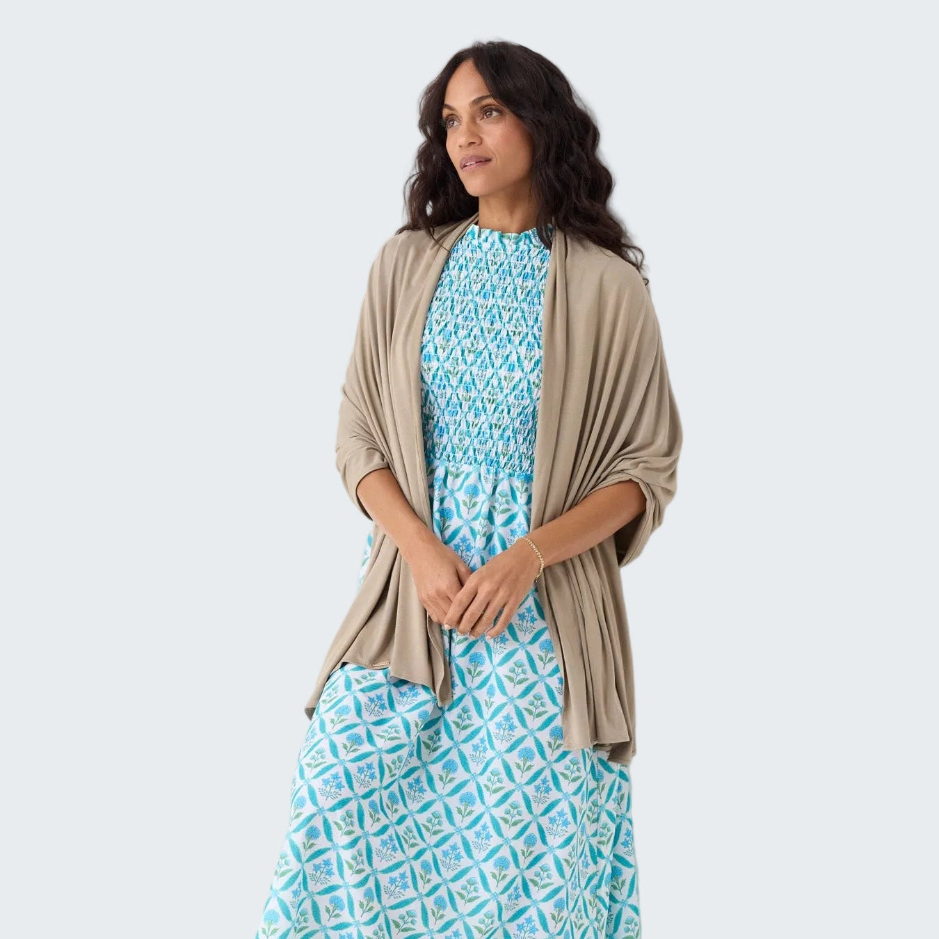 Woman wearing a blue patterned dress with a beige cardigan against a white background