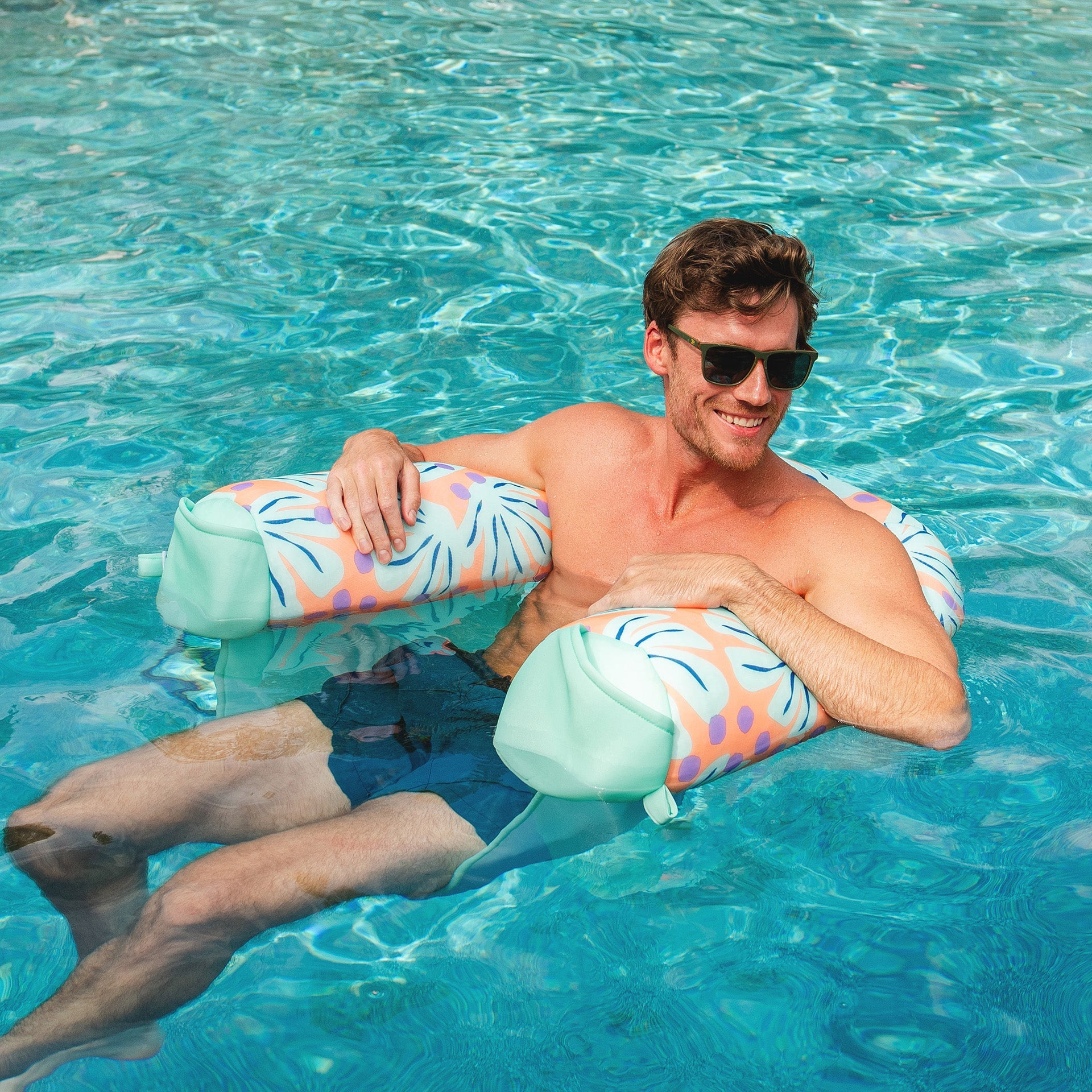 Man lounging on a colorful inflatable pool float in clear blue water