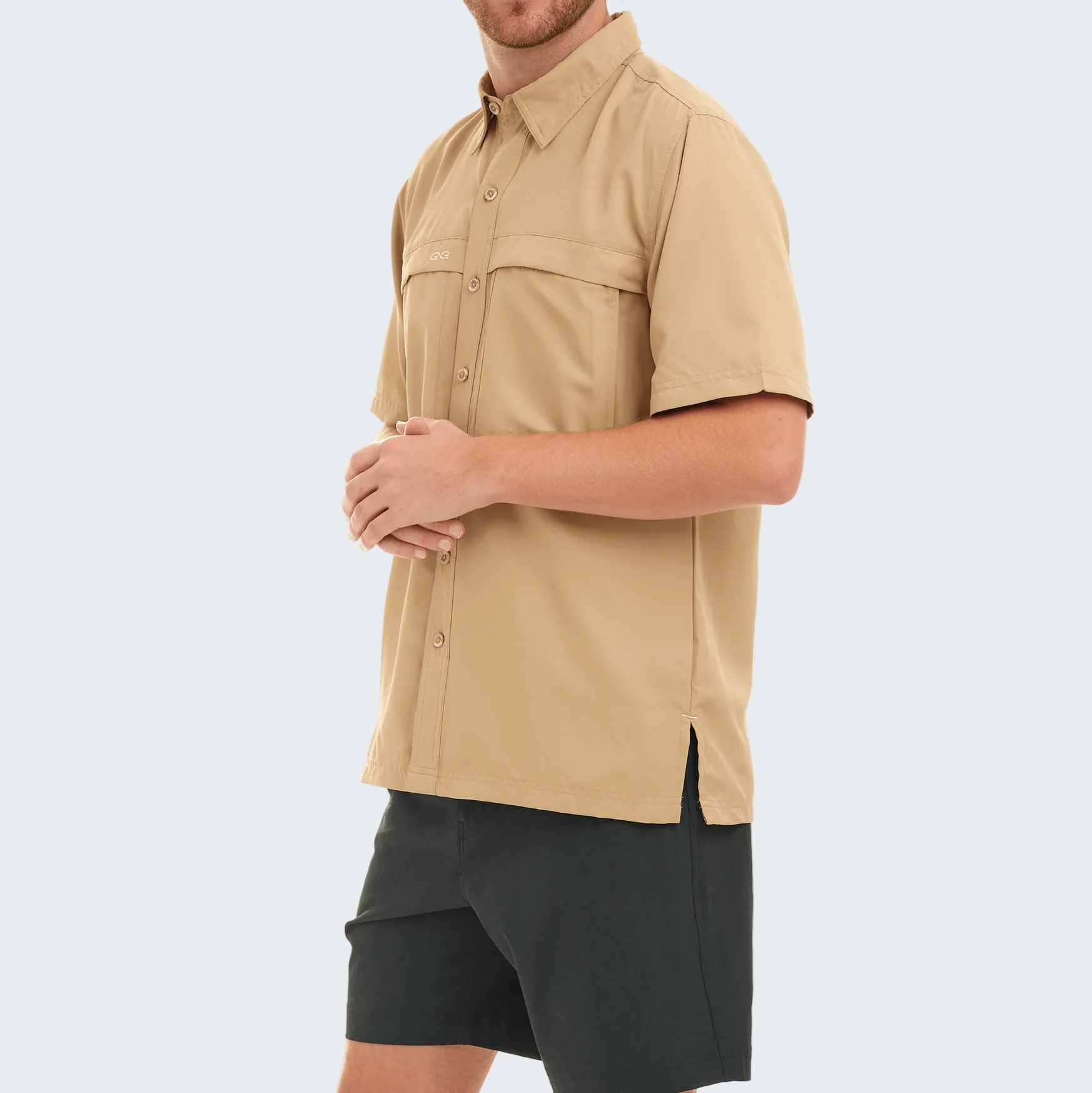 Man wearing a beige short-sleeve shirt and black shorts on a white background