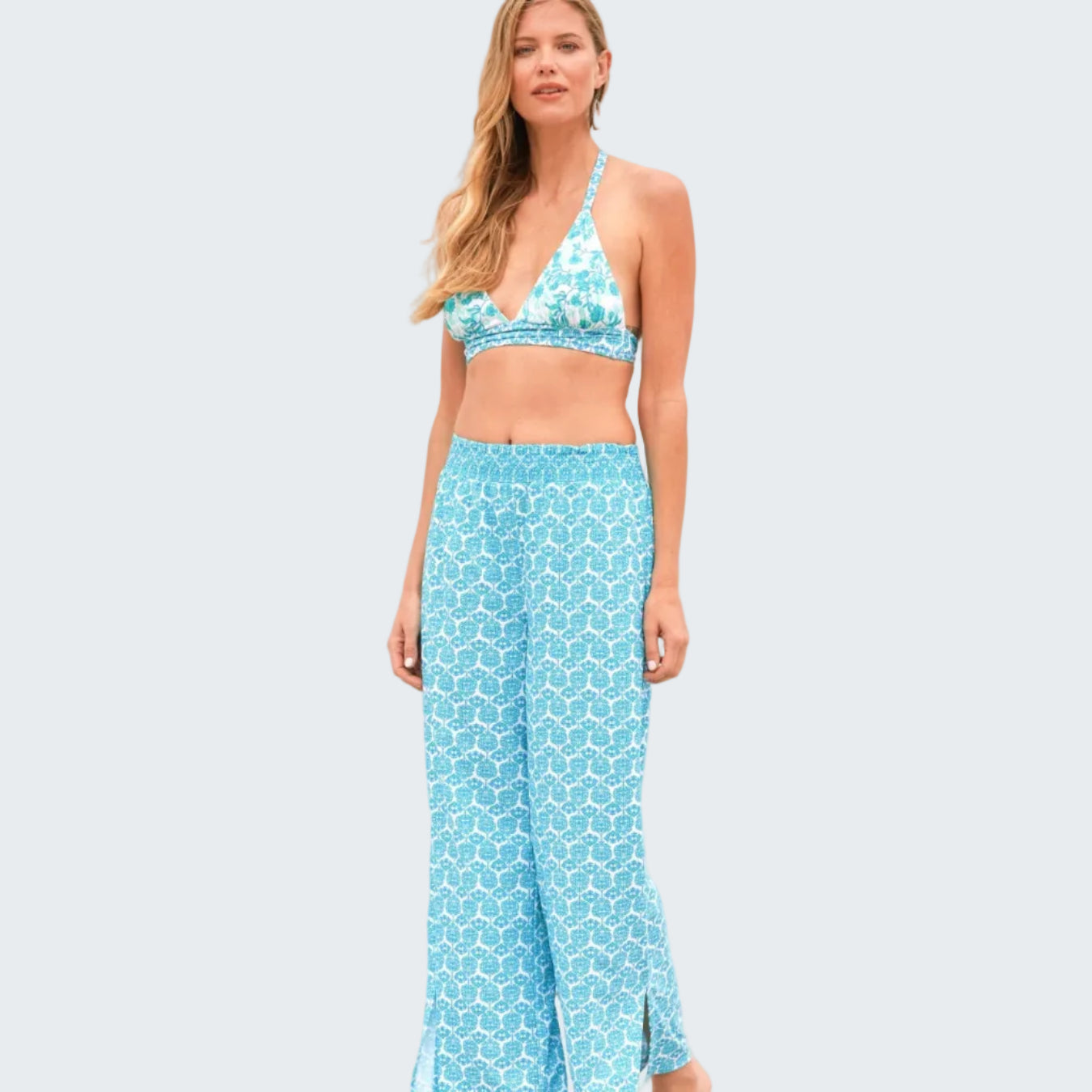 Woman wearing a blue patterned bikini and pants on a beach