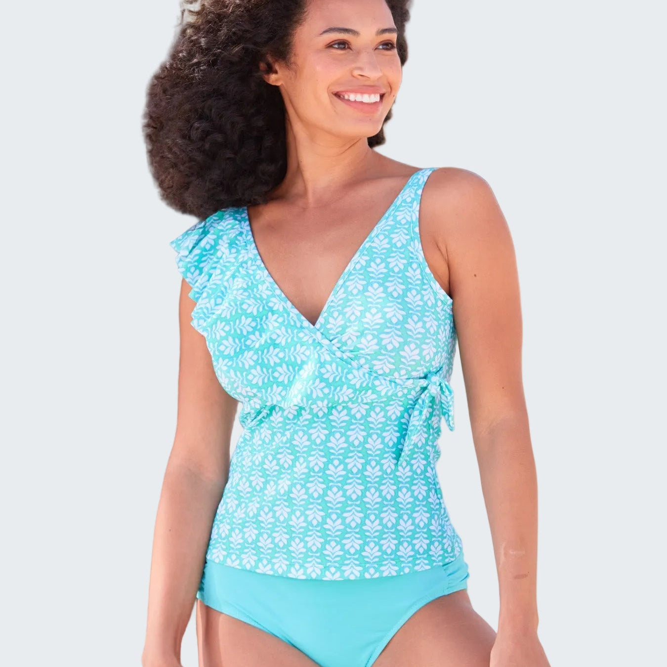 Woman in a blue swimsuit standing next to a palm tree on a beach.