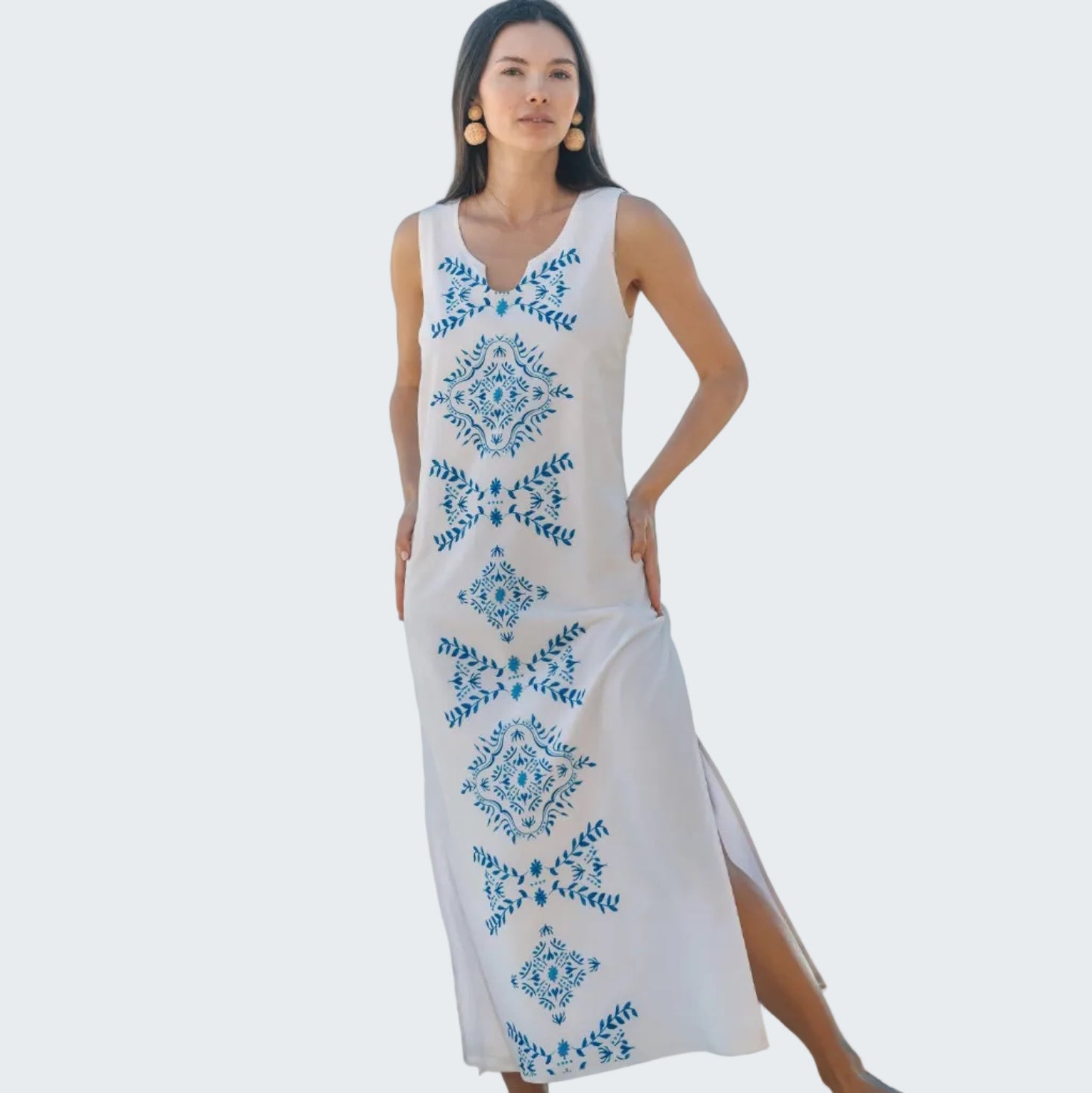 Woman wearing a white dress with blue floral patterns on a beach.