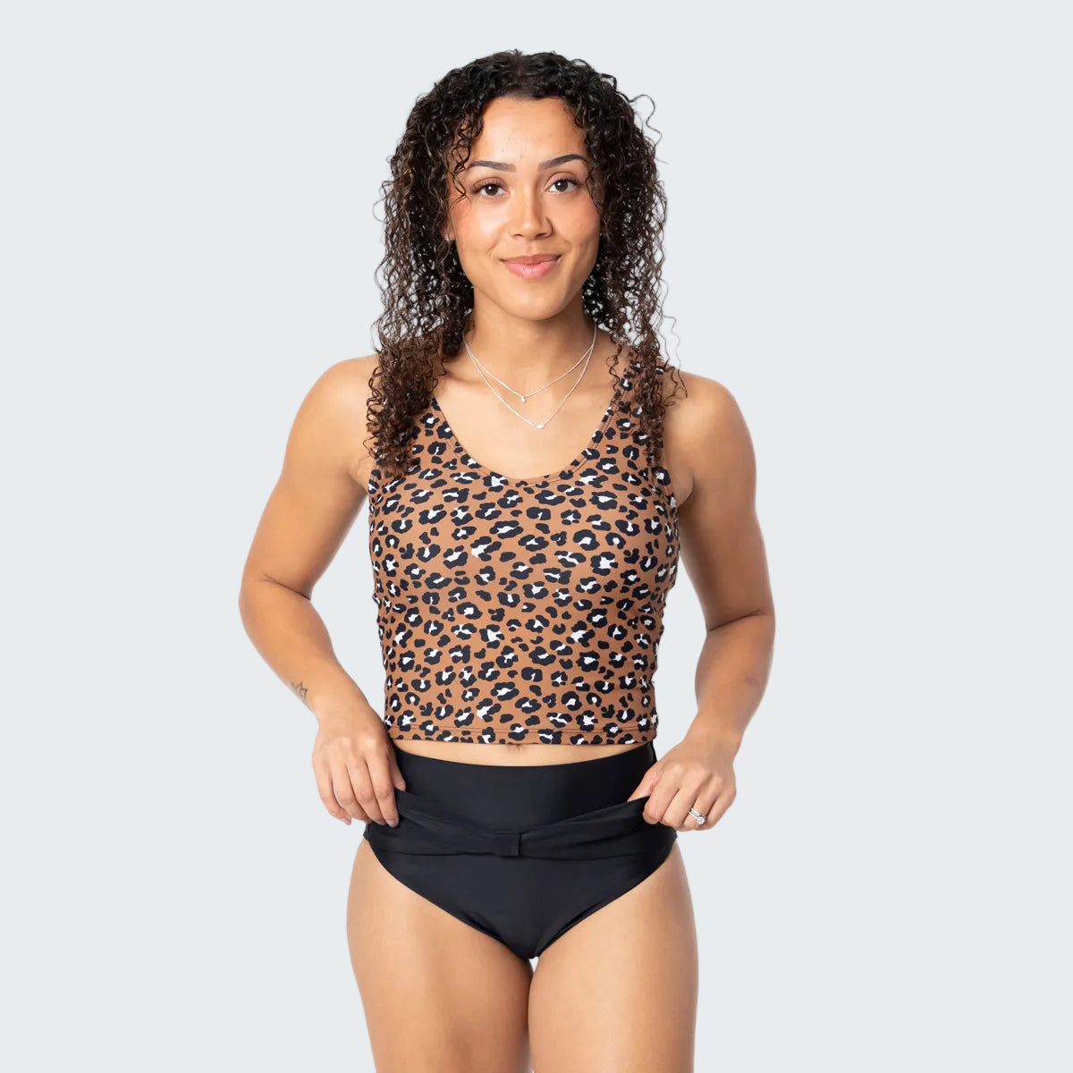 Woman wearing a leopard print top and black high-waisted bikini bottoms on a white background