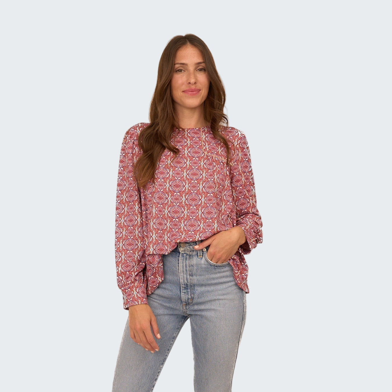 Woman wearing a patterned blouse and jeans on a white background