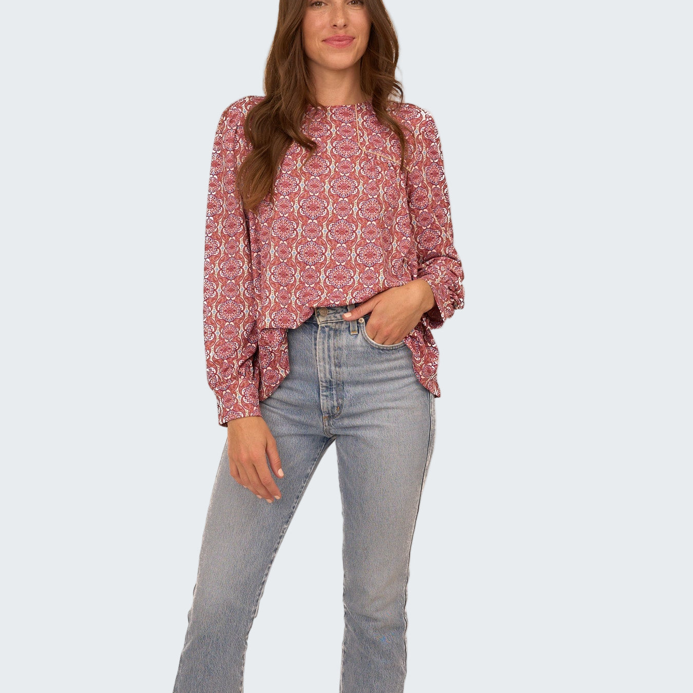 Woman wearing a patterned blouse and jeans on a white background