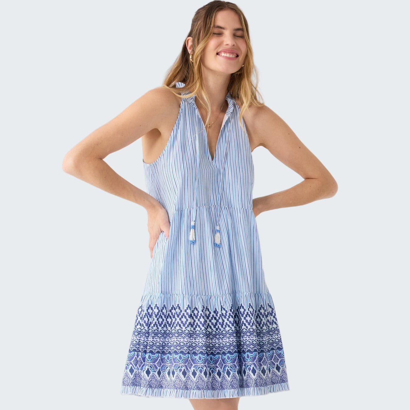 Woman wearing a blue and white striped dress with a geometric hem on a white background