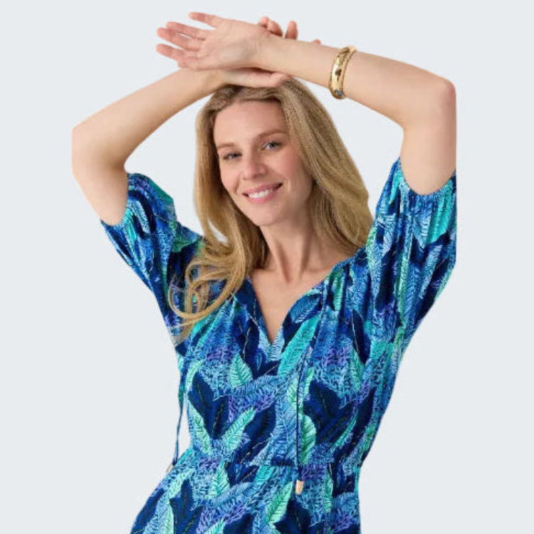 Woman wearing a blue patterned dress with her arms raised against a plain background