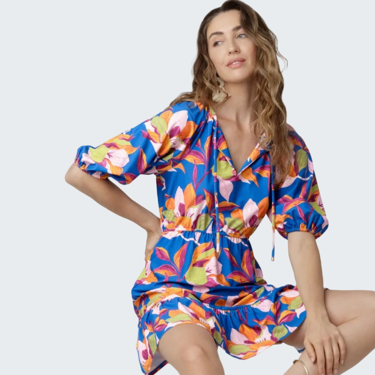 Woman wearing a colorful floral dress sitting on a white box against a white background