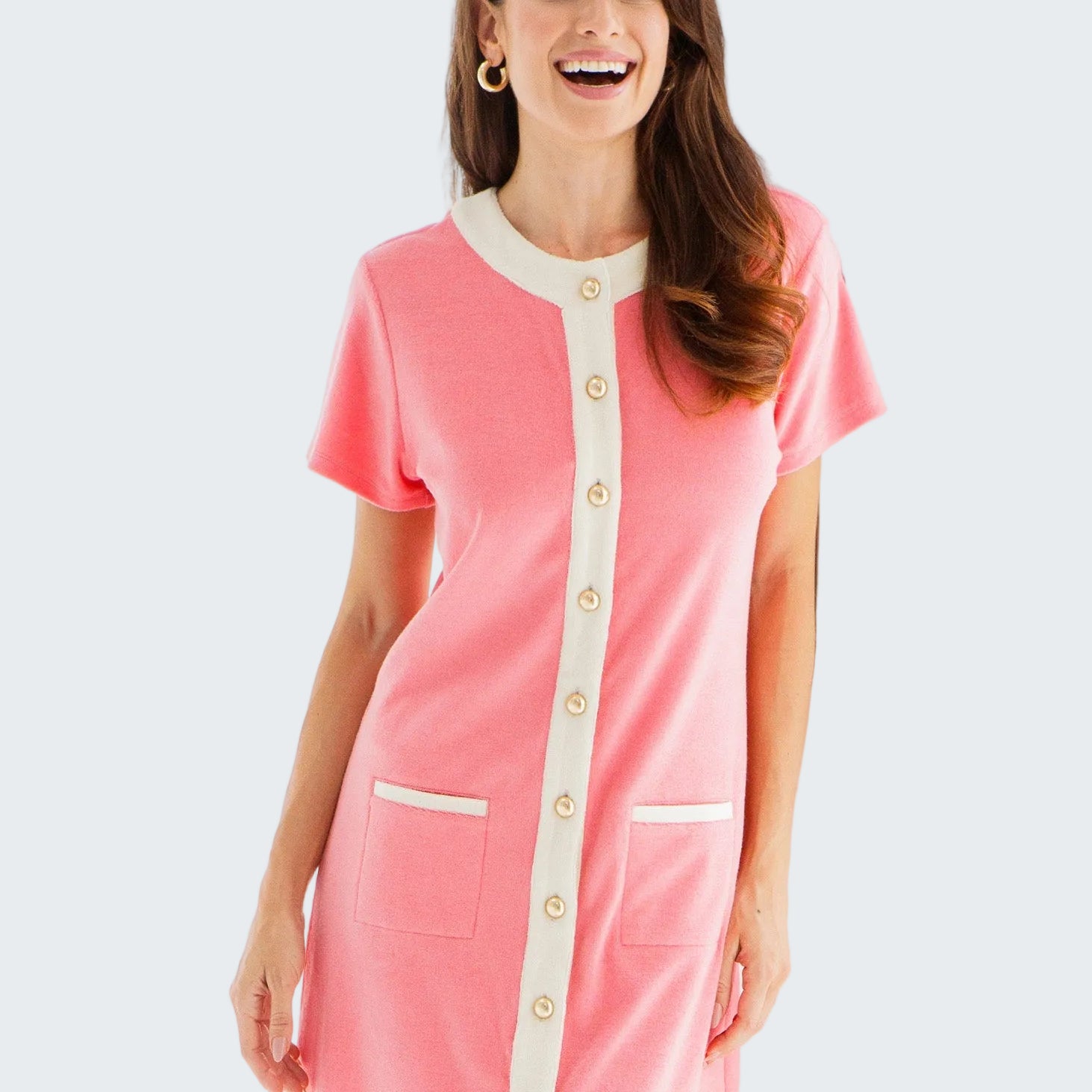 Woman wearing a pink dress with white accents standing in a bright room.