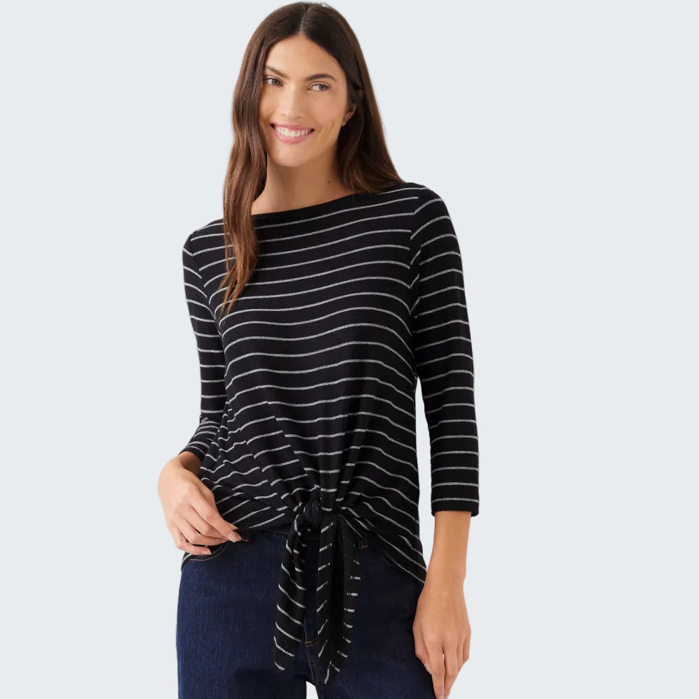 A woman modeling a black and white horizontally striped long-sleeve top with a side-tie detail, paired with dark blue jeans, against a plain light gray background.