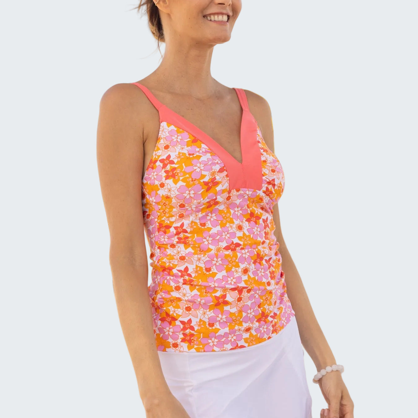 Woman wearing a colorful floral tank top and white skirt on a beach with palm trees in the background.