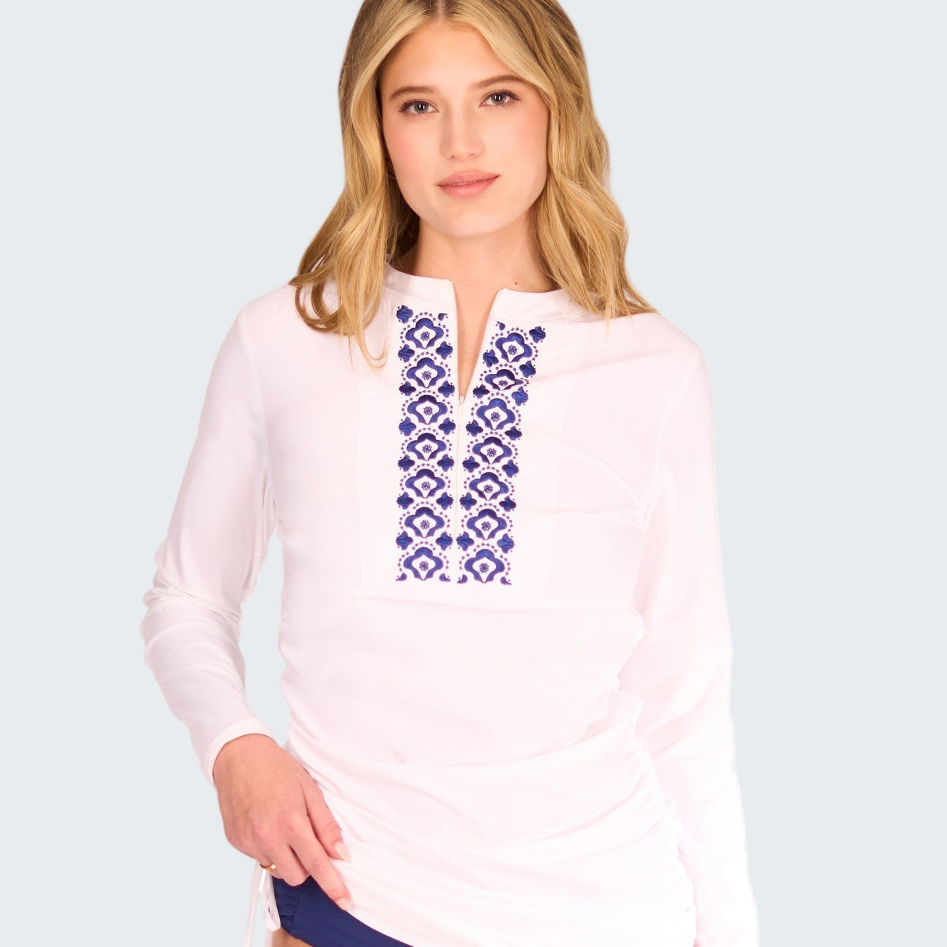 Woman wearing a white long-sleeve top with blue embroidery and matching blue bottoms on a white background