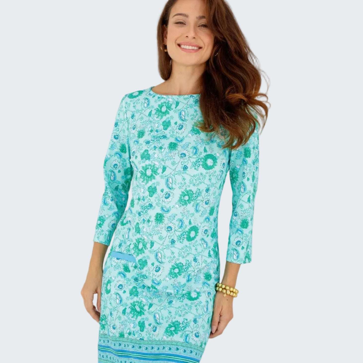Woman wearing a turquoise floral dress standing in front of a white window.