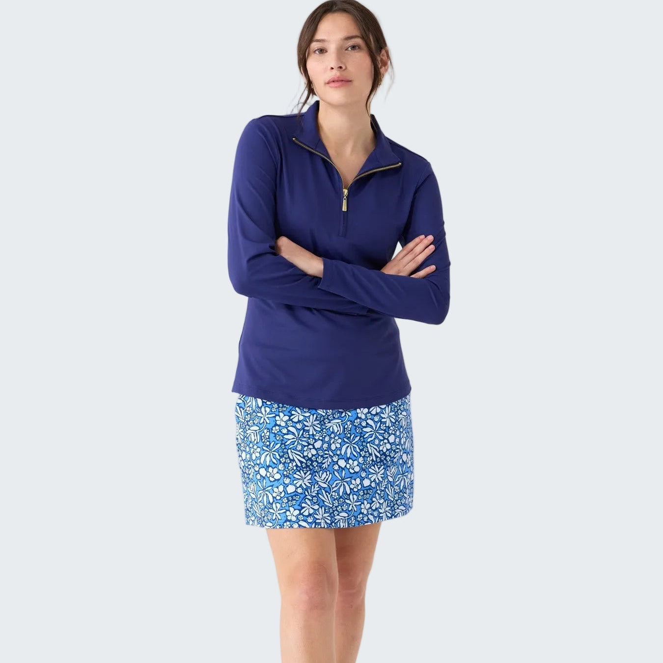 Woman wearing a blue quarter-zip top and floral skirt on a white background