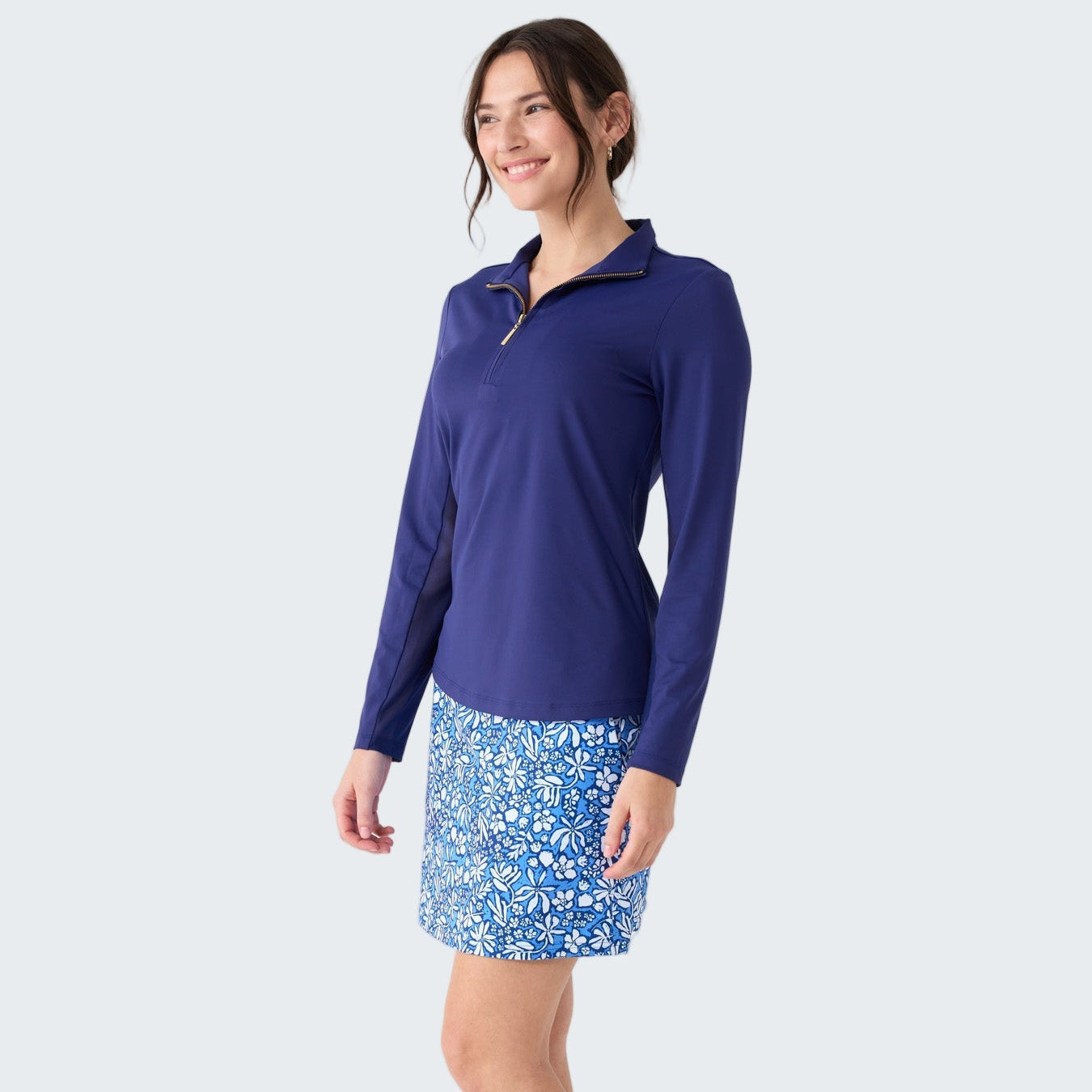Woman wearing a blue long-sleeve top and floral skirt on a white background