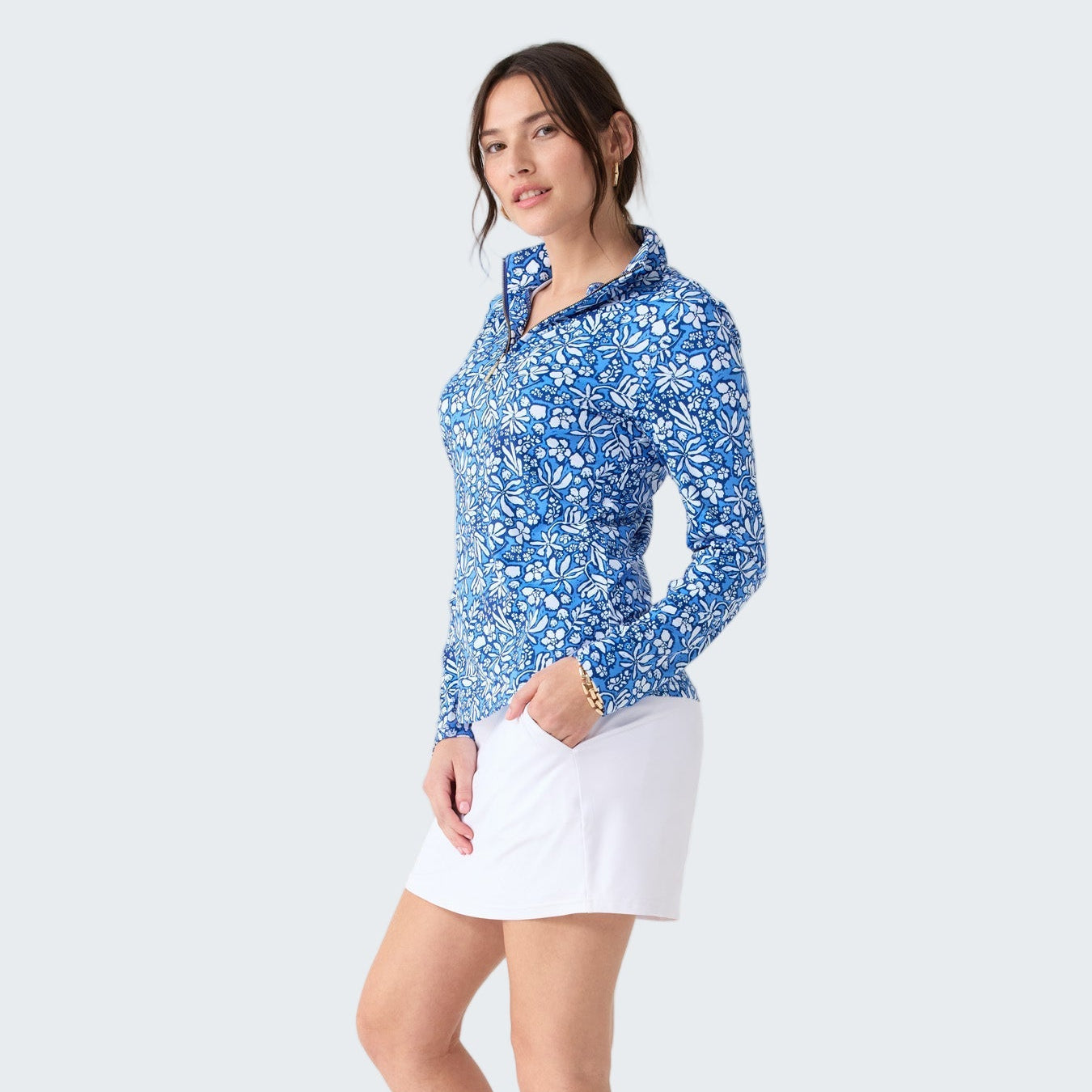 Woman wearing a blue floral long-sleeve shirt and white skirt on a white background