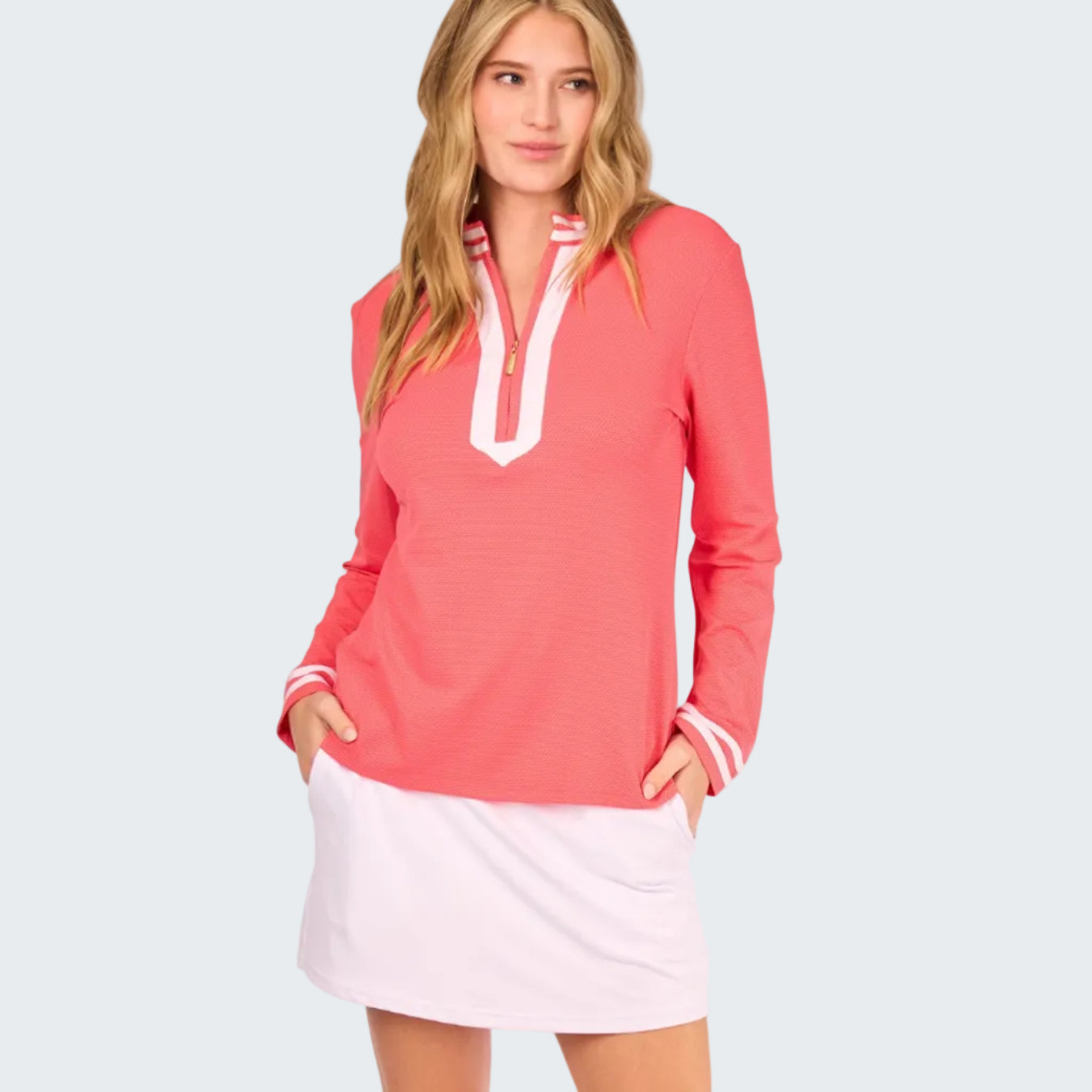 Woman wearing a coral long-sleeve top with white trim and a white skirt on a white background