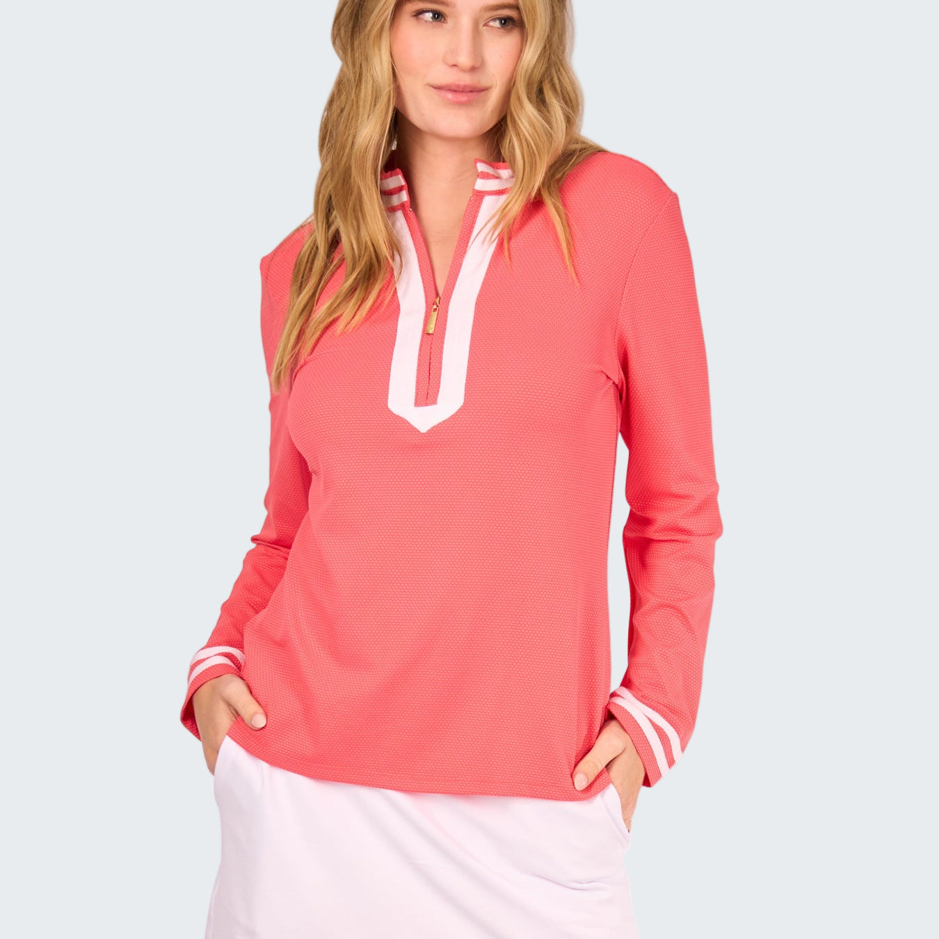 Woman wearing a coral long-sleeve top with white trim and a white skirt on a white background