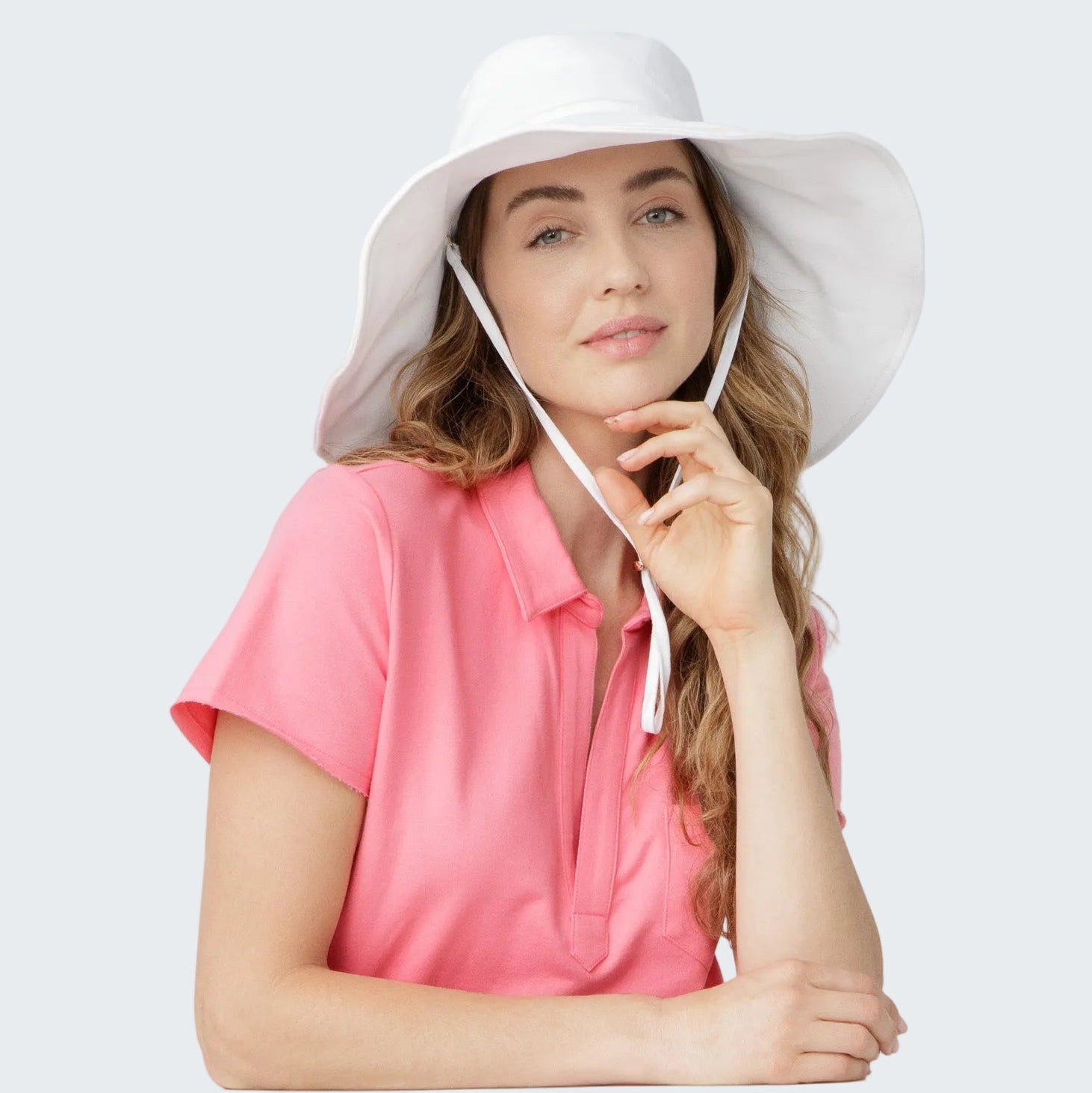 Woman wearing a white sun hat and pink shirt on a light gray background