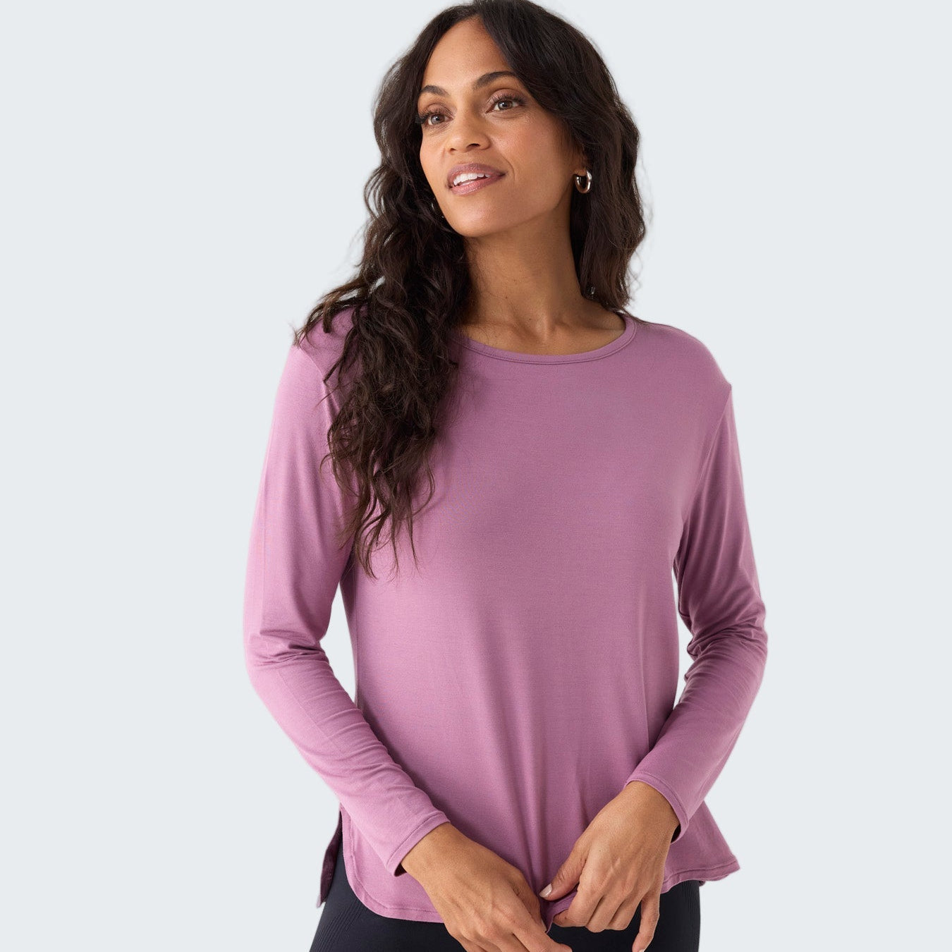 Woman wearing a pink long-sleeve top and black leggings on a white background