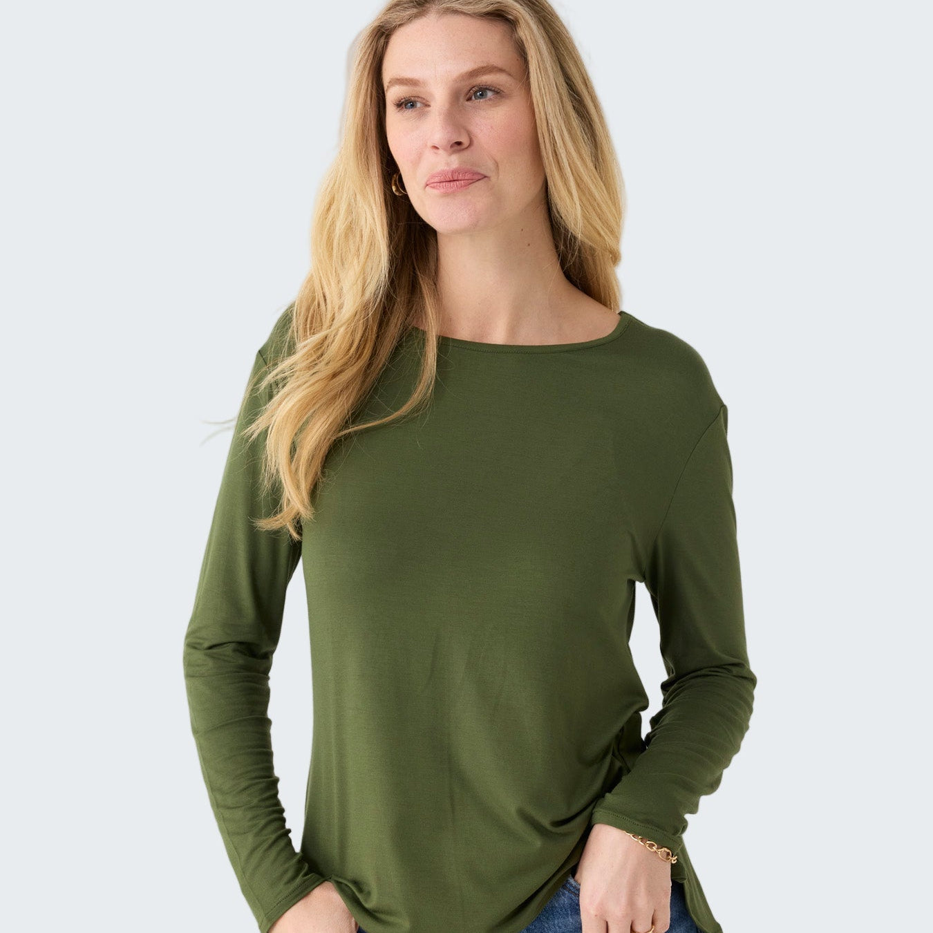 Woman wearing an olive green long-sleeve top and blue jeans on a white background
