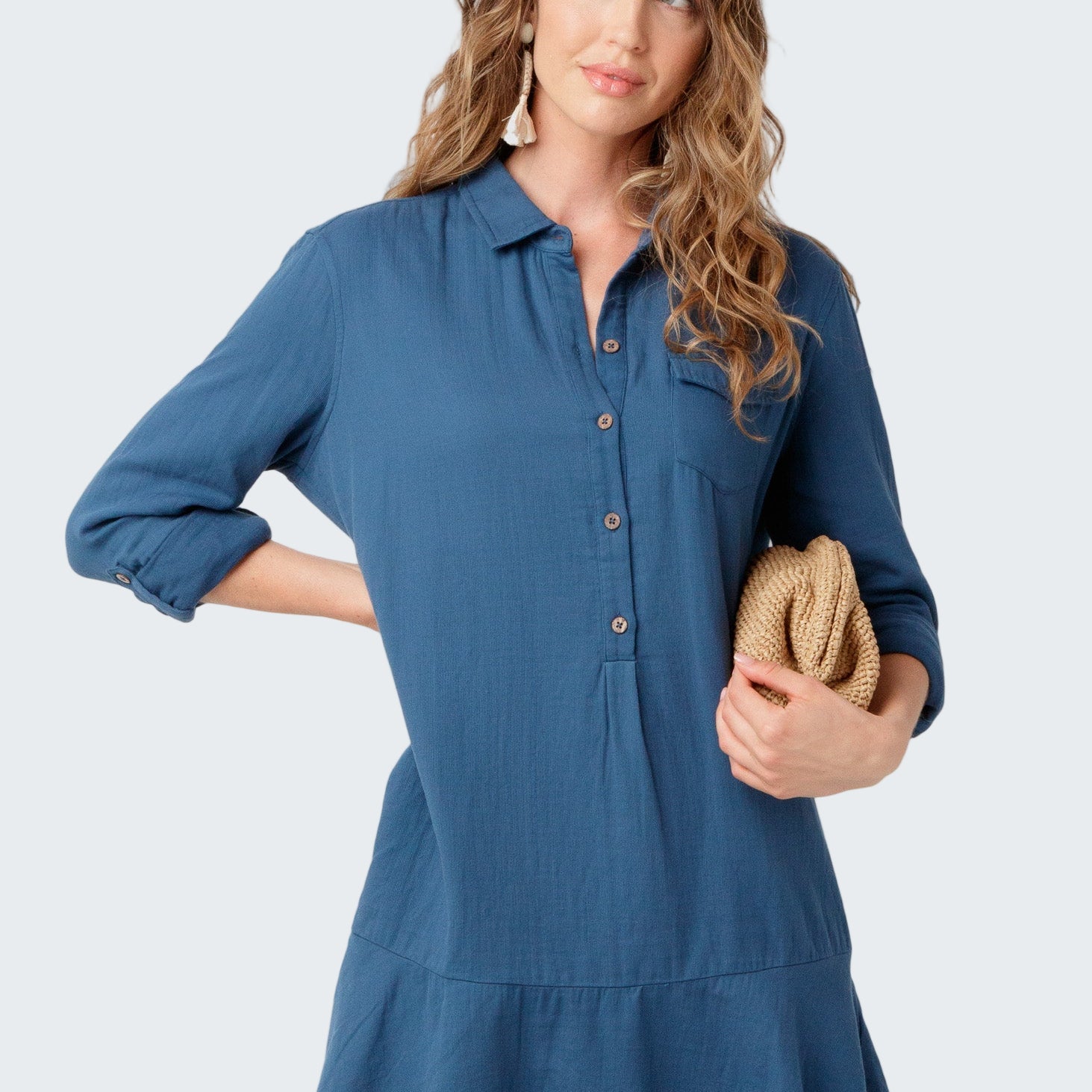 Woman wearing a blue dress holding a clutch against a white background