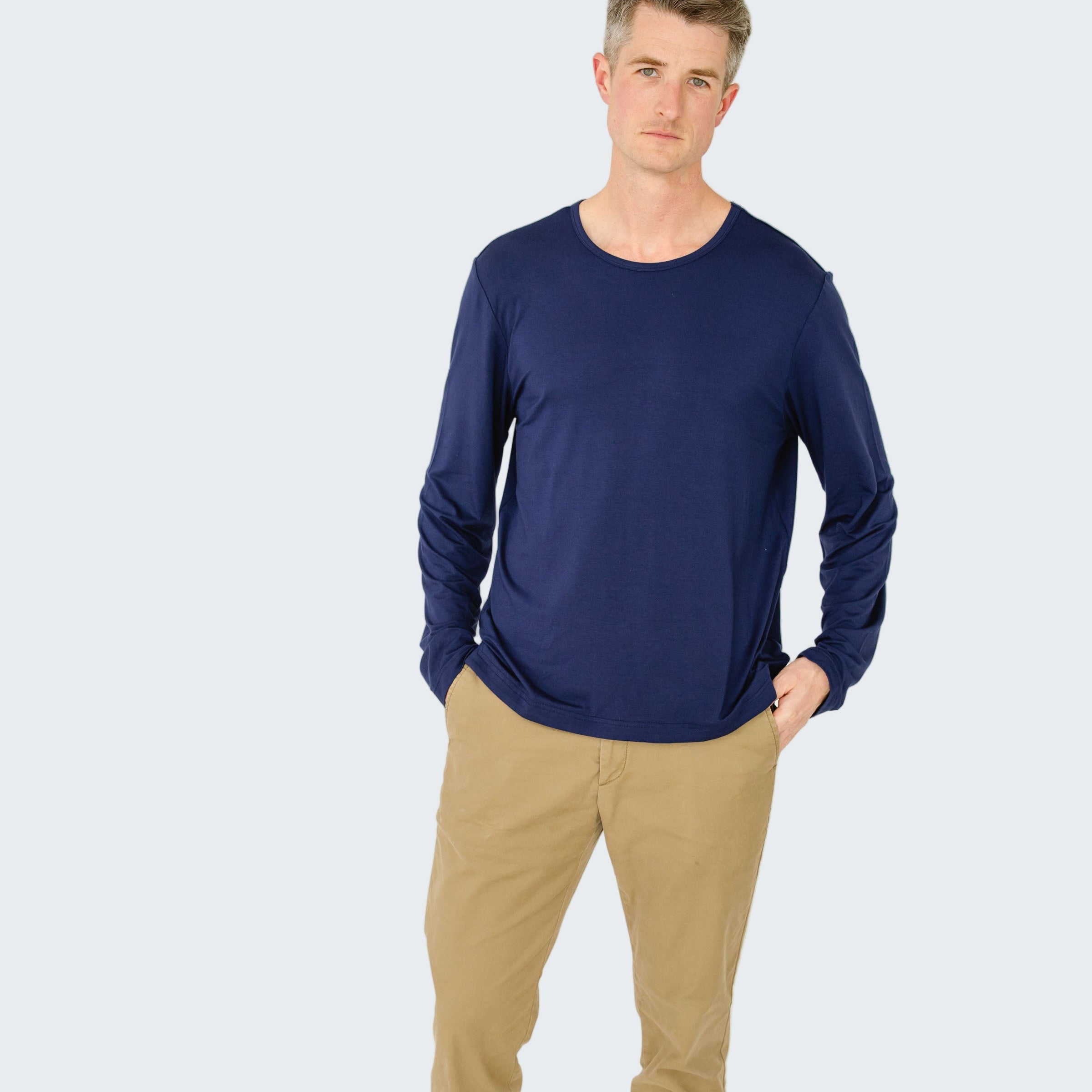 Man wearing a blue long-sleeve shirt and beige pants on a white background