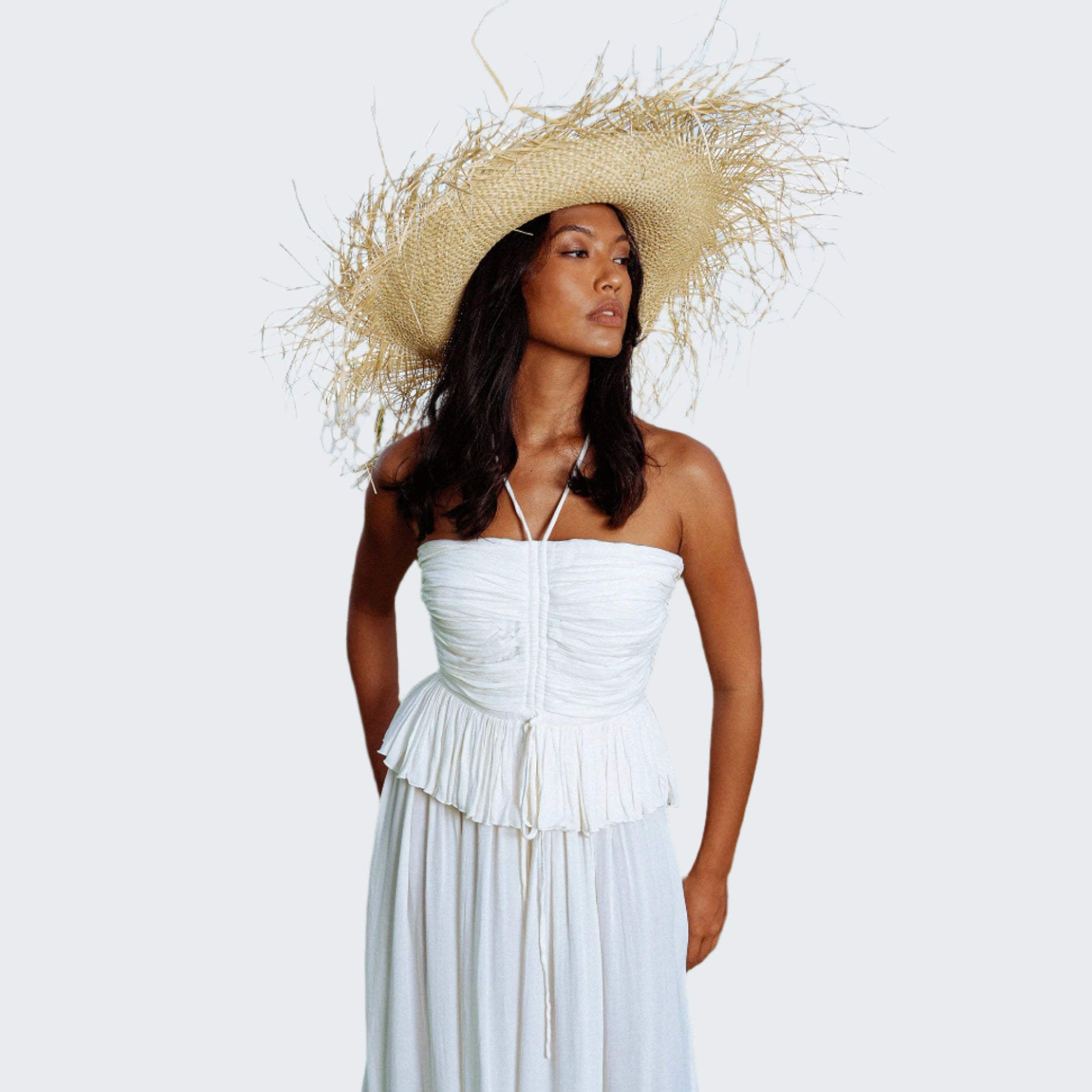 Woman in a white dress and straw hat standing outdoors with ocean in the background
