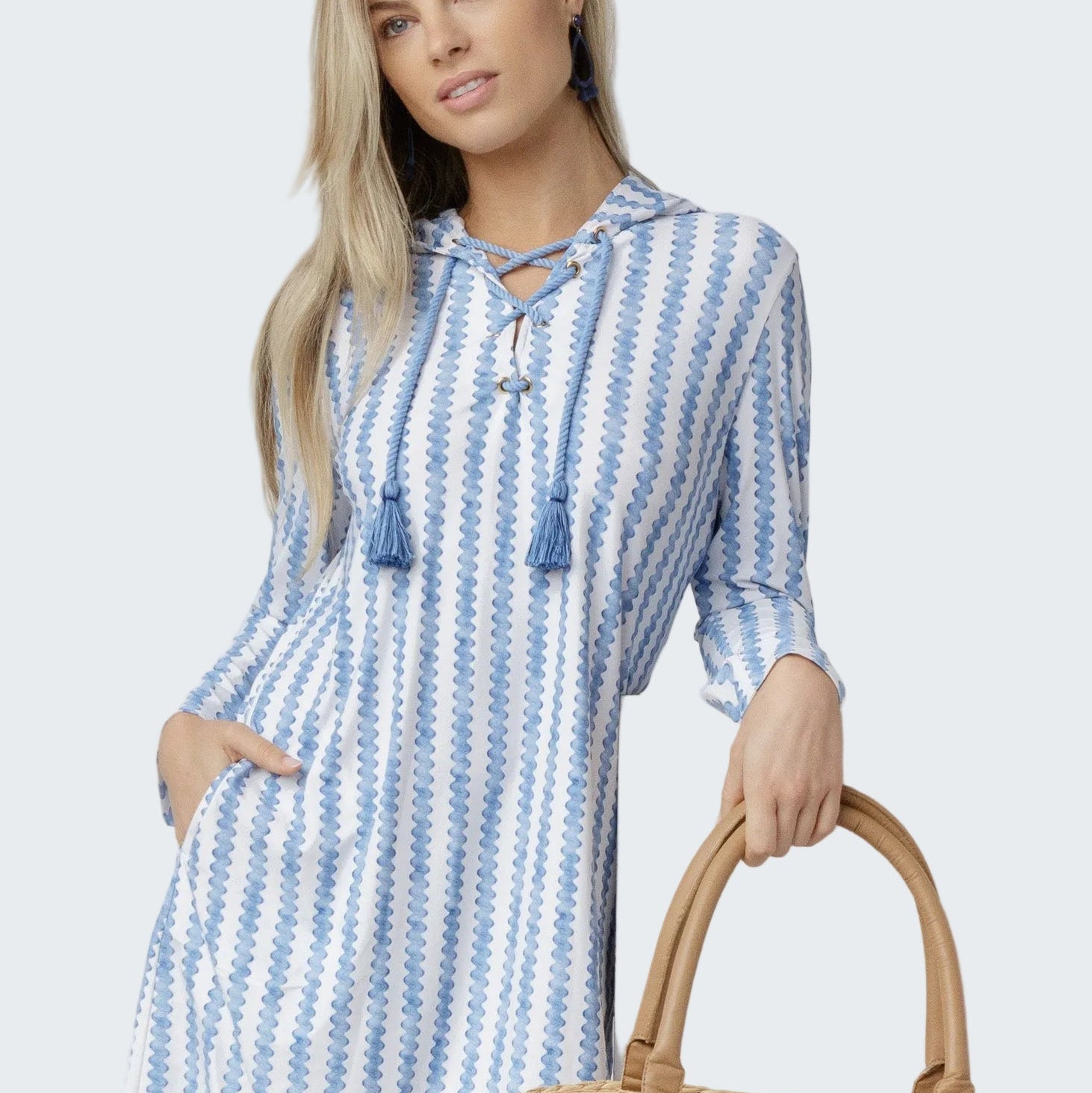 Woman wearing a blue and white striped dress holding a straw bag against a white background