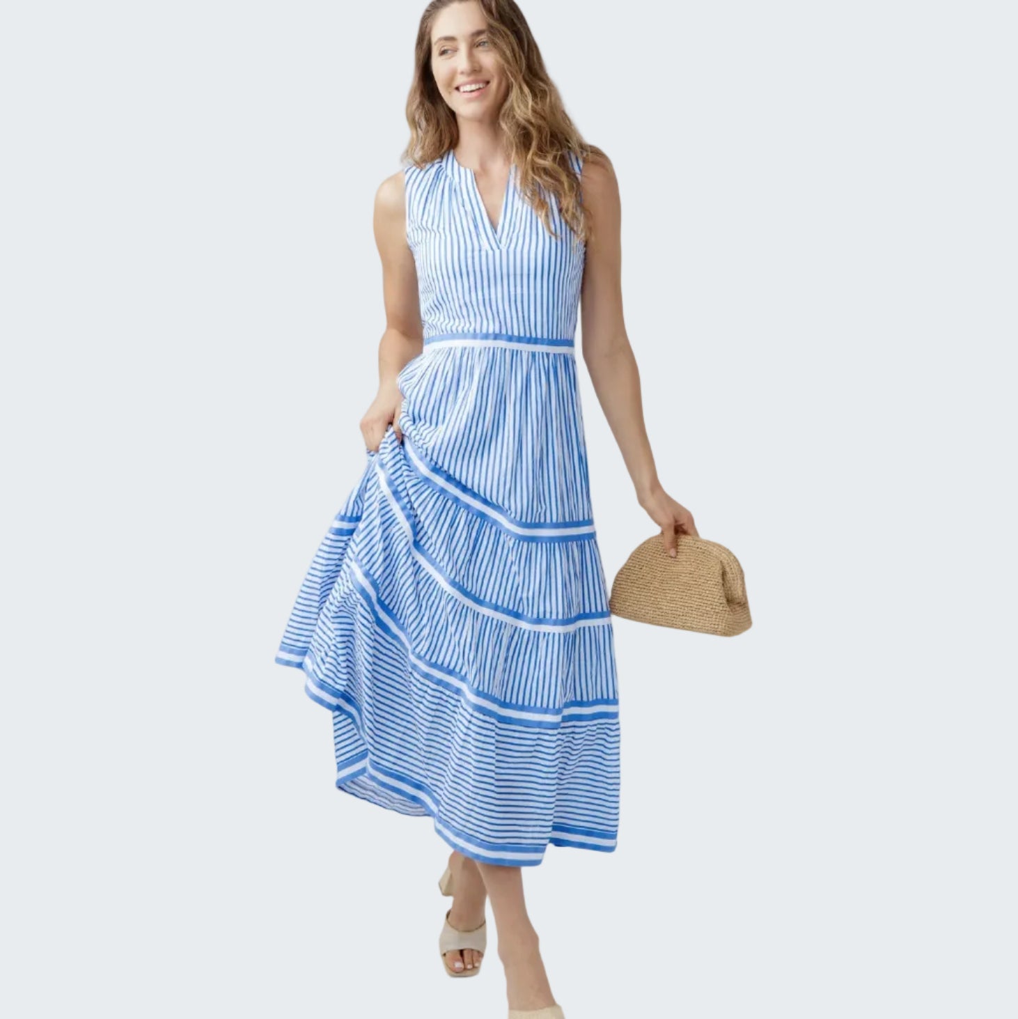Woman wearing a blue and white striped dress holding a straw bag on a white background
