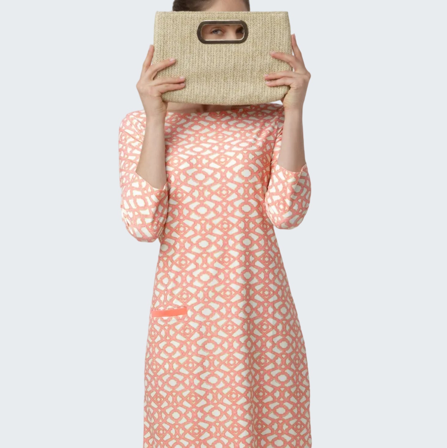 Woman wearing a patterned dress holding a woven bag against a white background