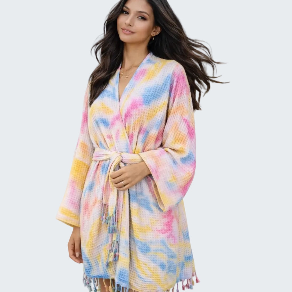 Woman wearing a colorful robe on a beach with ocean and house in the background