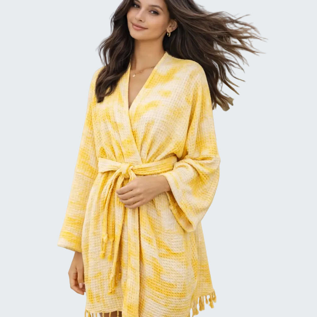 Woman wearing a yellow and white patterned robe on a beach.