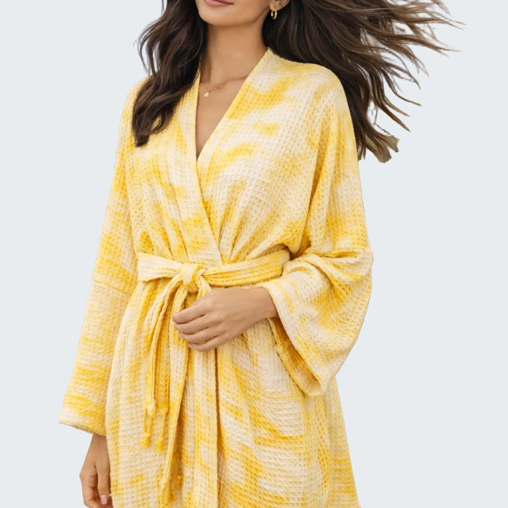 Woman wearing a yellow and white patterned robe on a beach.
