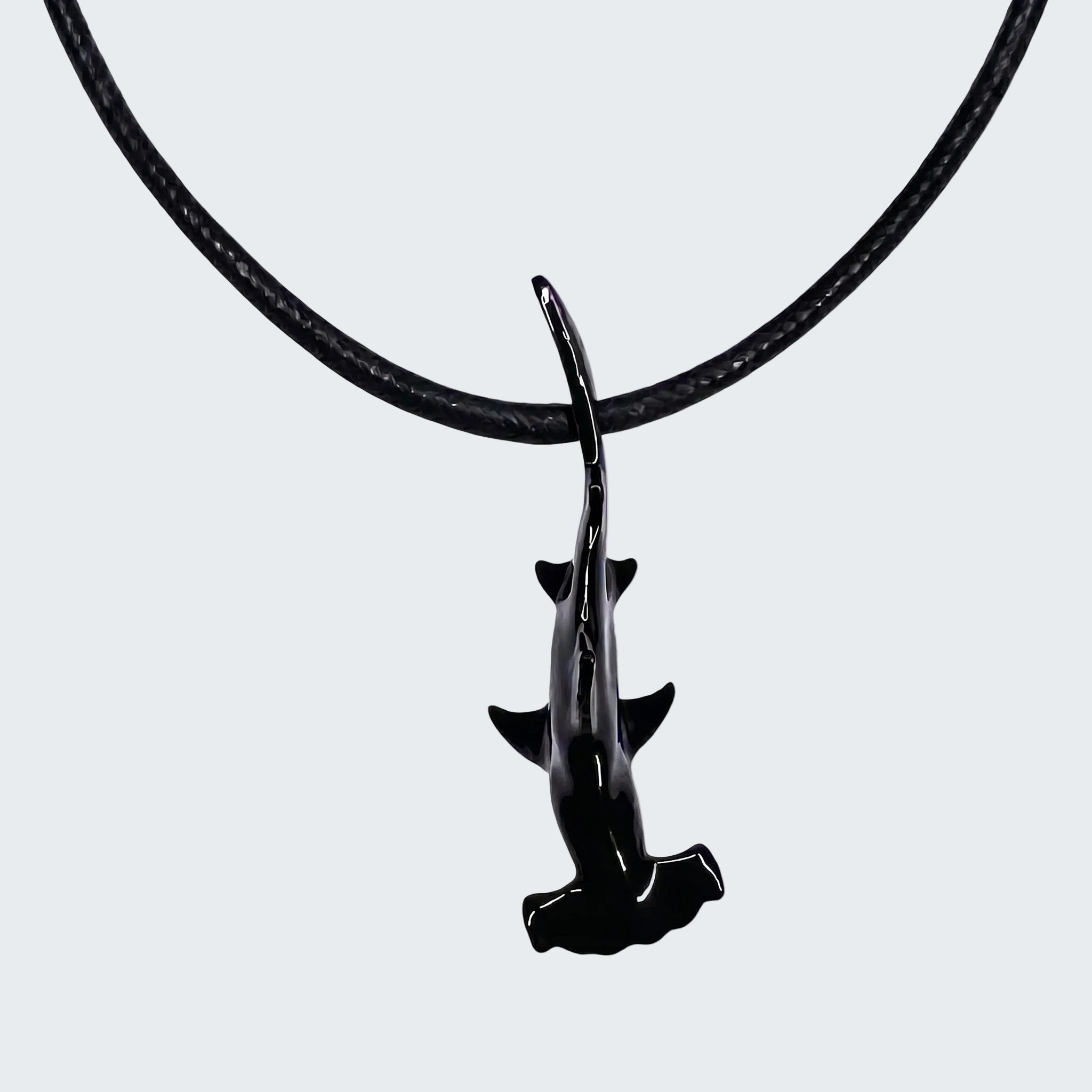 Black shark pendant on a black cord against a white background