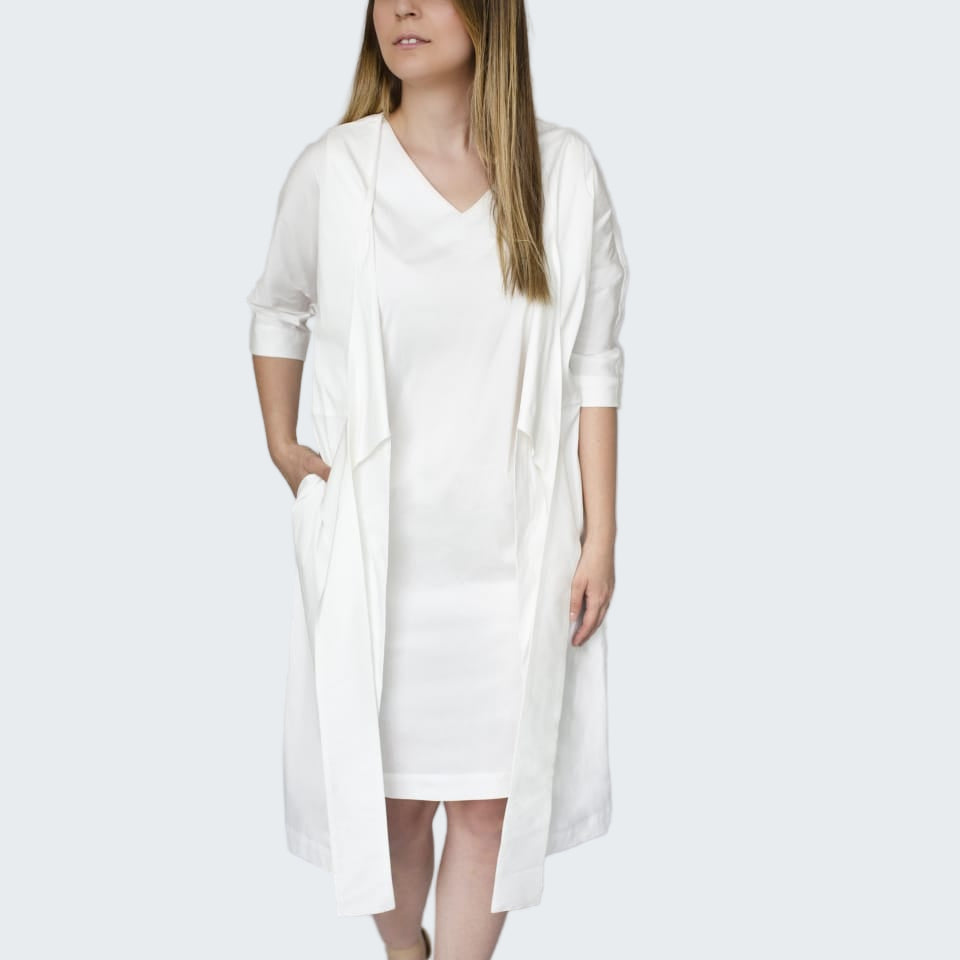 Woman wearing a white dress and cardigan against a plain background