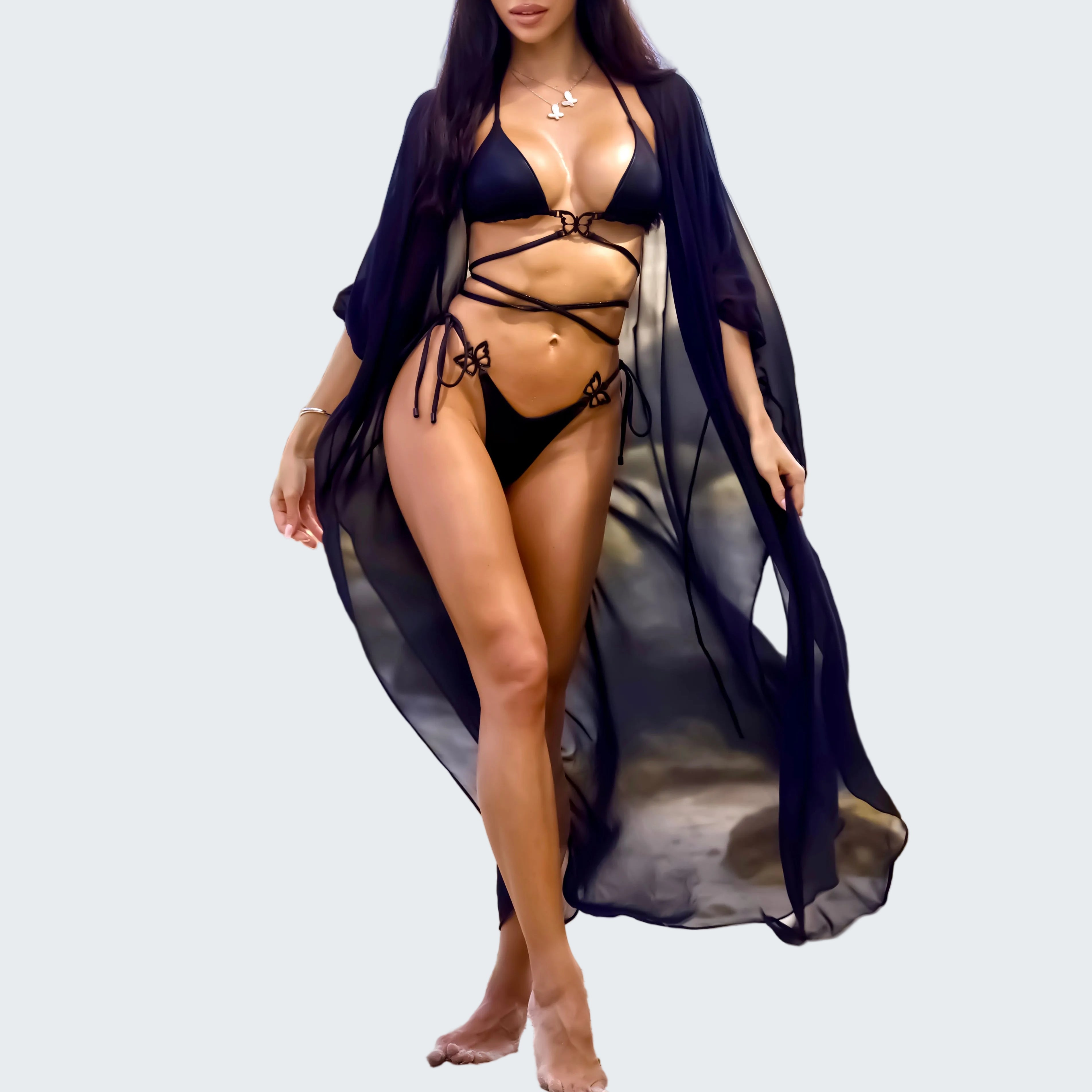 Woman in a black bikini and blue cover-up standing on a rocky beach with ocean in the background