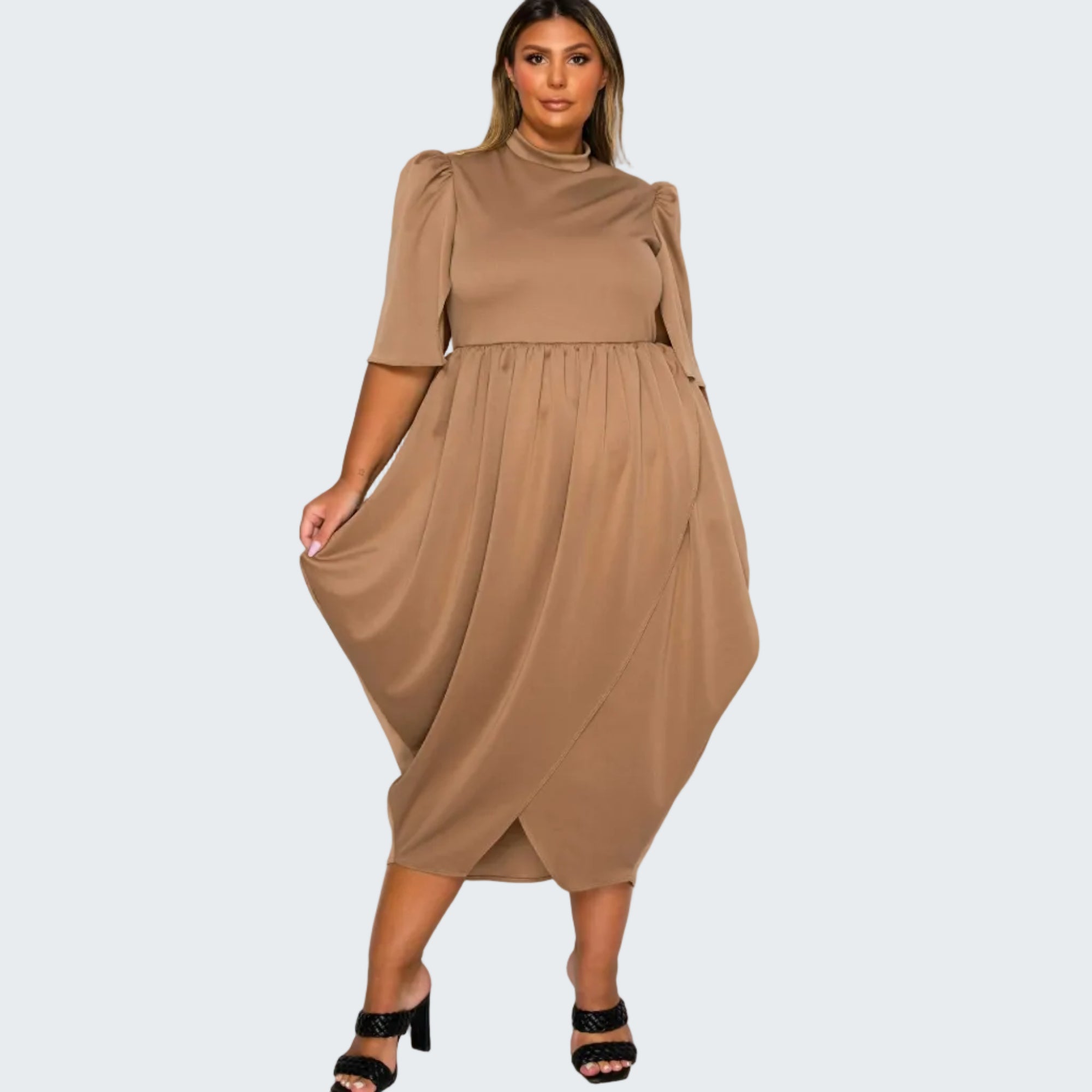 A woman modeling a taupe brown midi dress with puff sleeves, a mock neck, and an asymmetrical draped hem, paired with black heeled sandals against a plain white background.