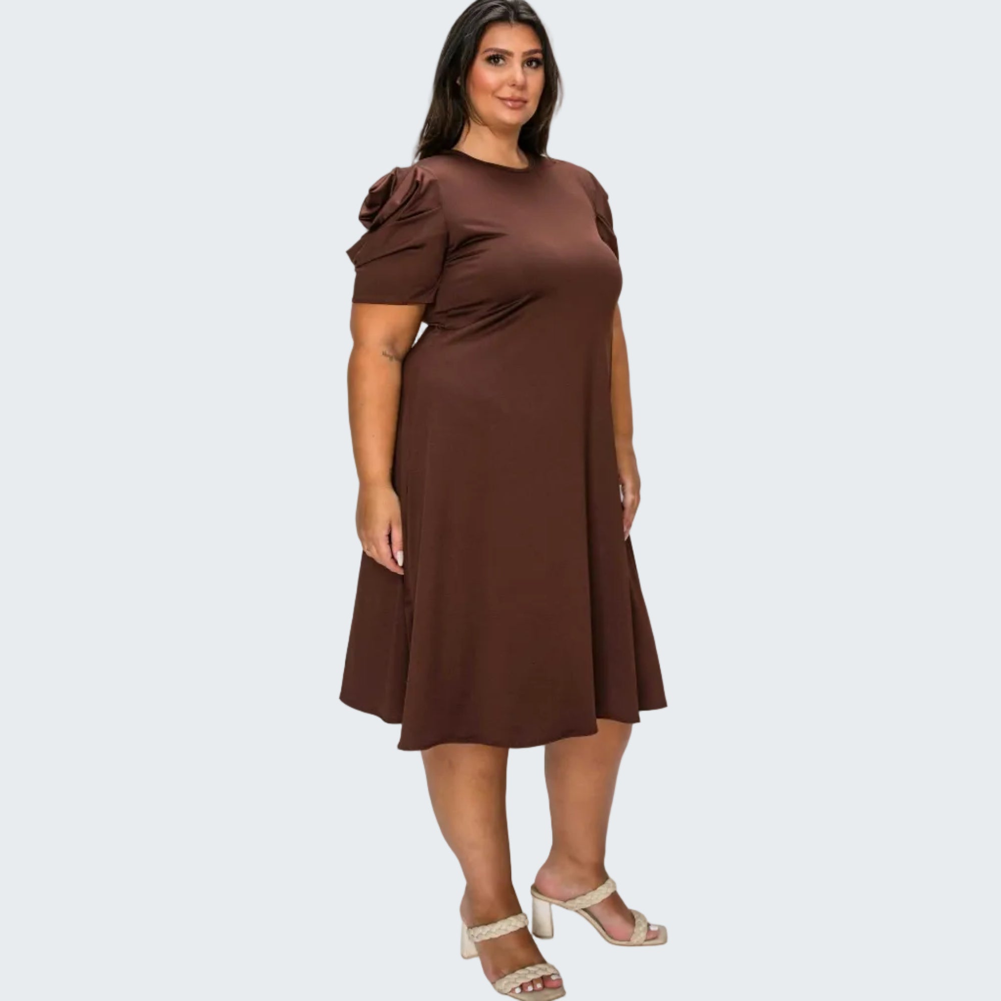 A woman modeling a brown short-sleeve dress with a ruffled shoulder detail, standing against a plain white background.