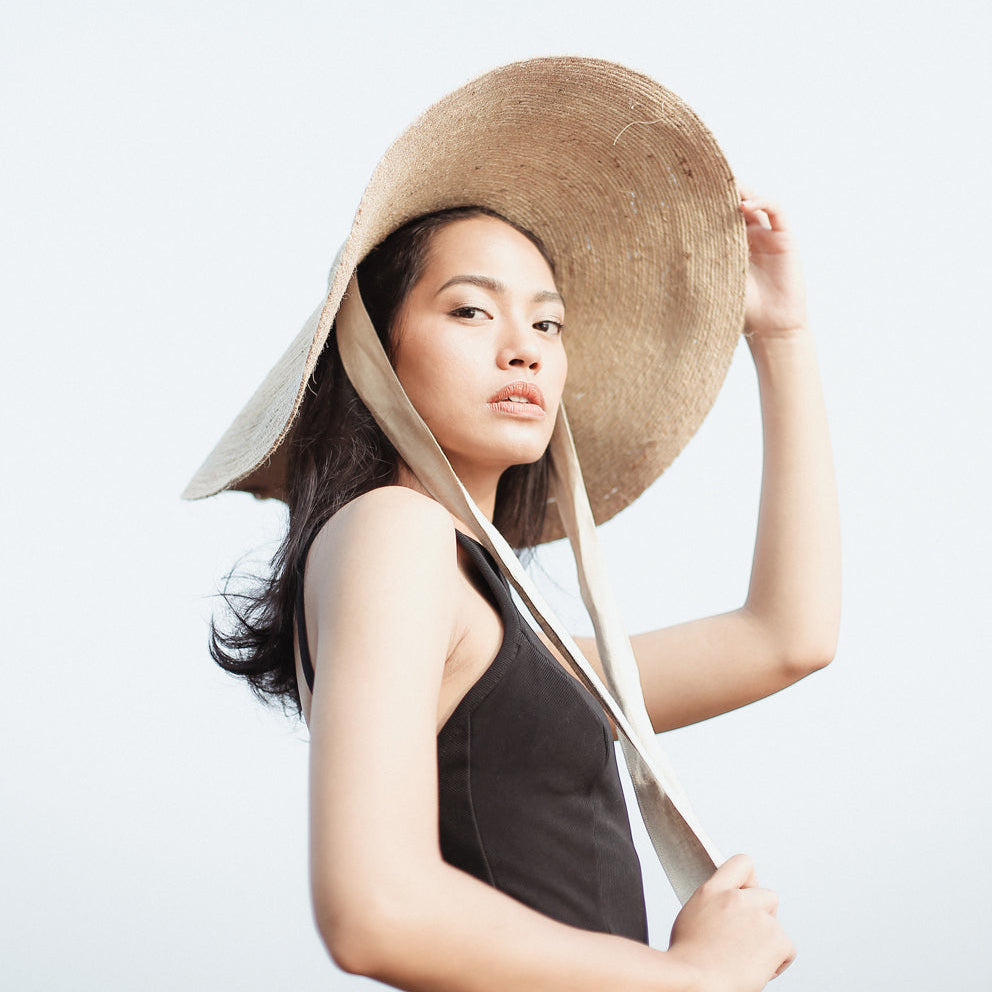 Woman wearing a large straw hat against a plain background